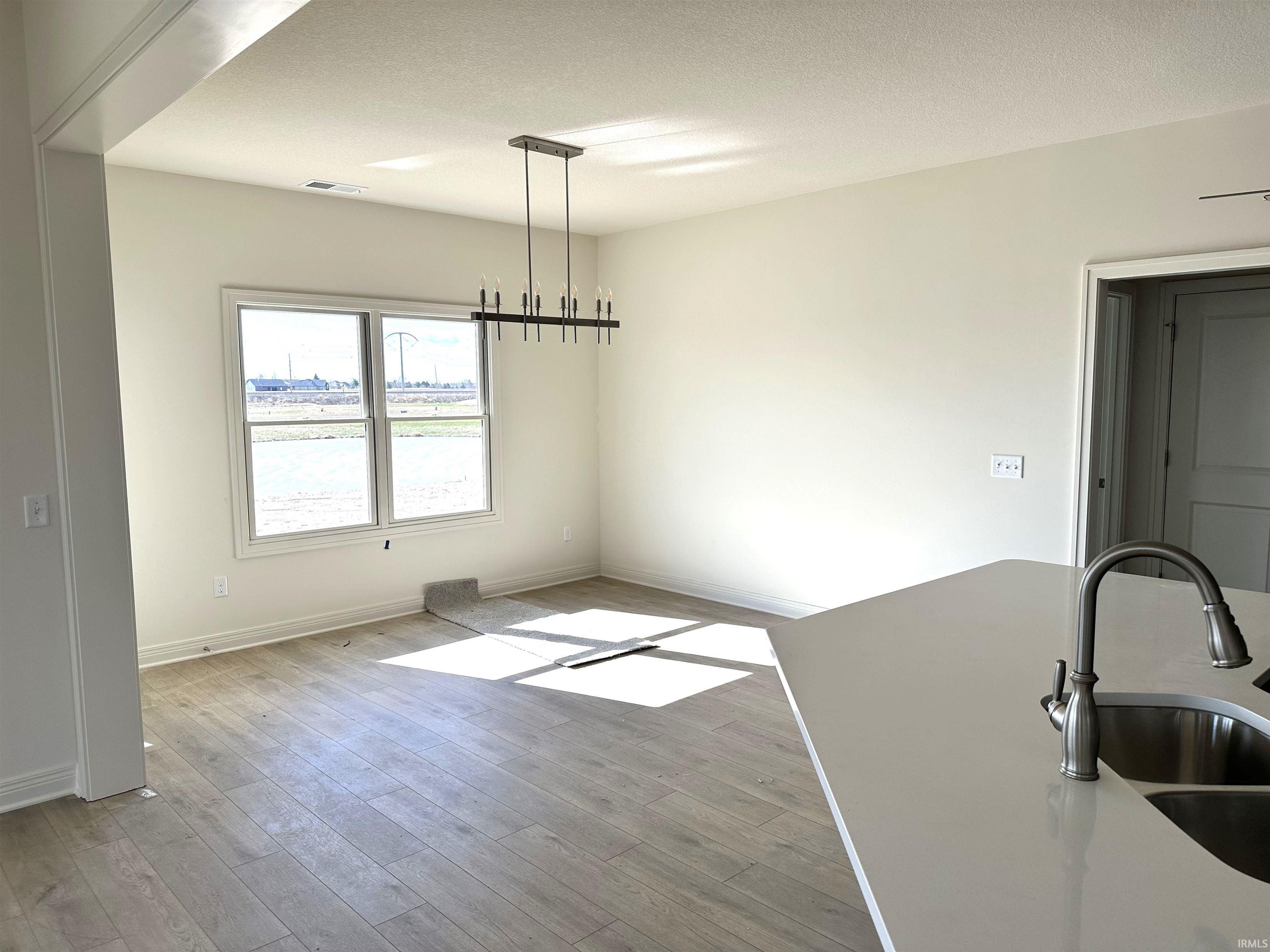 Unfurnished dining area featuring light wood-style flooring, hanging lights, and a textured ceiling