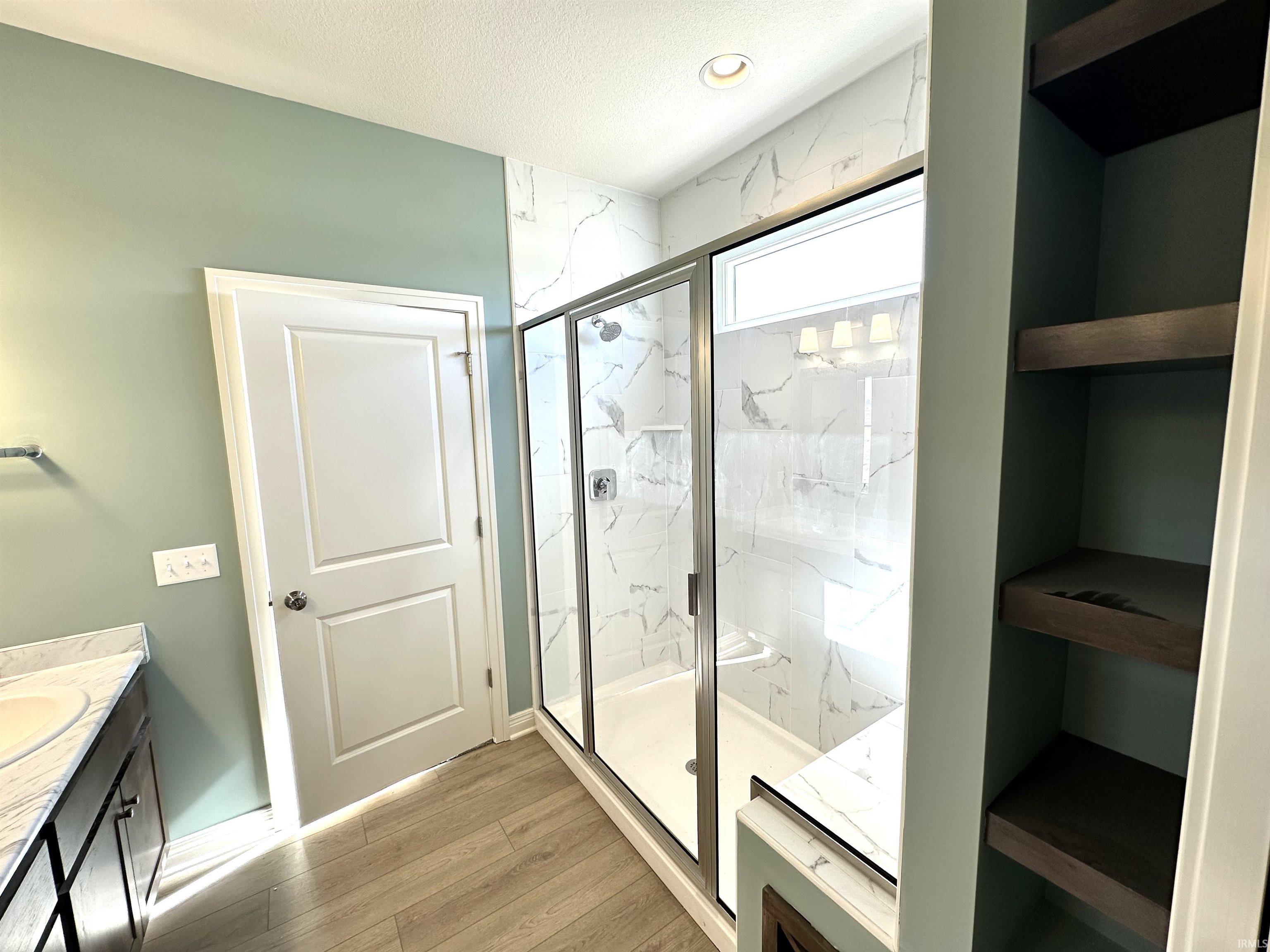 Full bathroom featuring vanity, a marble finish shower, light wood finished floors, and recessed lighting