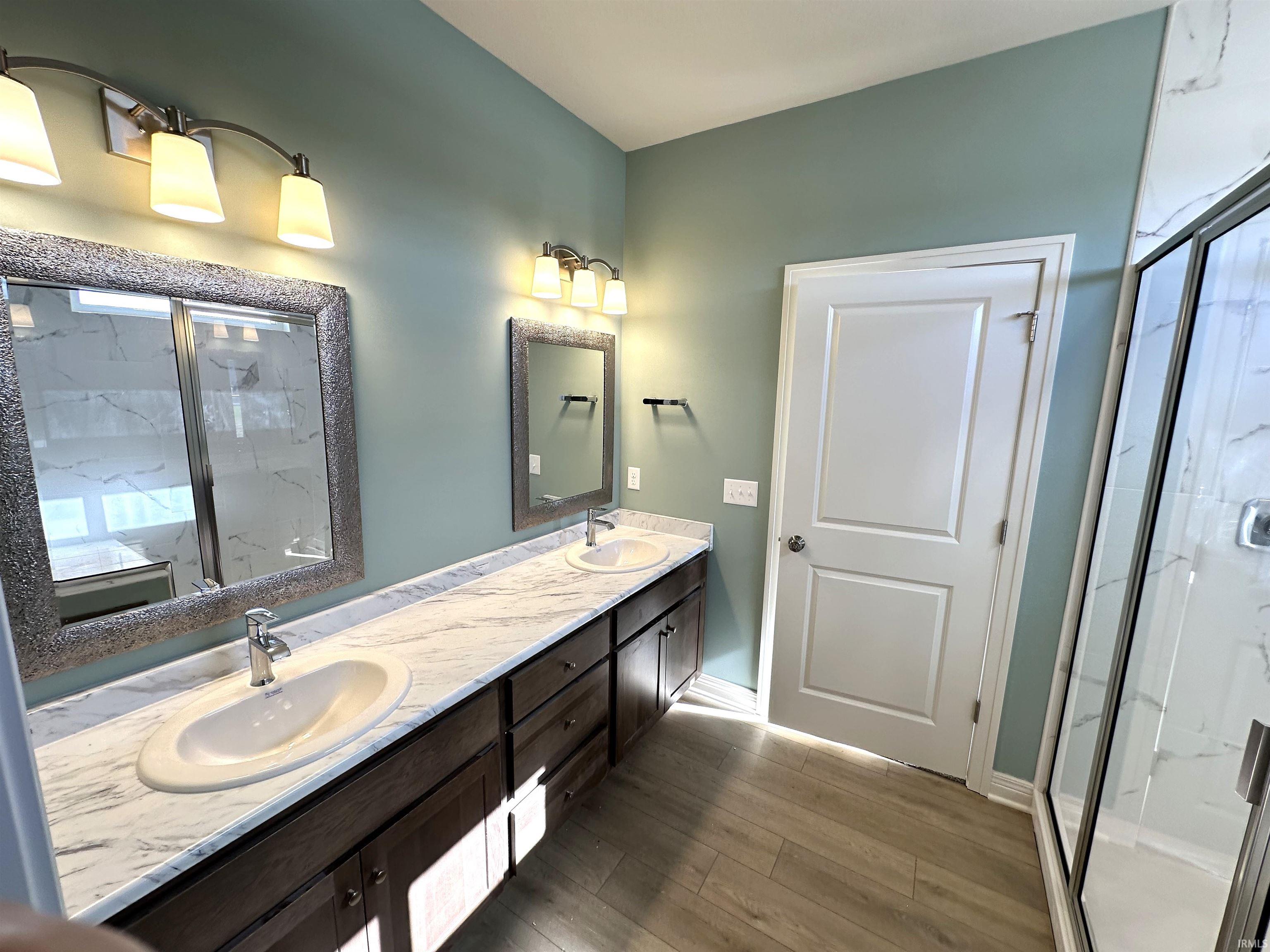 Full bath with a marble finish shower, double vanity, and light wood-style floors