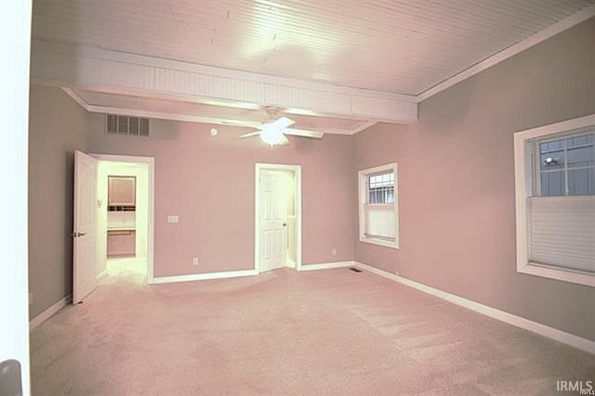 Empty room featuring light carpet, ceiling fan, beam ceiling, and crown molding