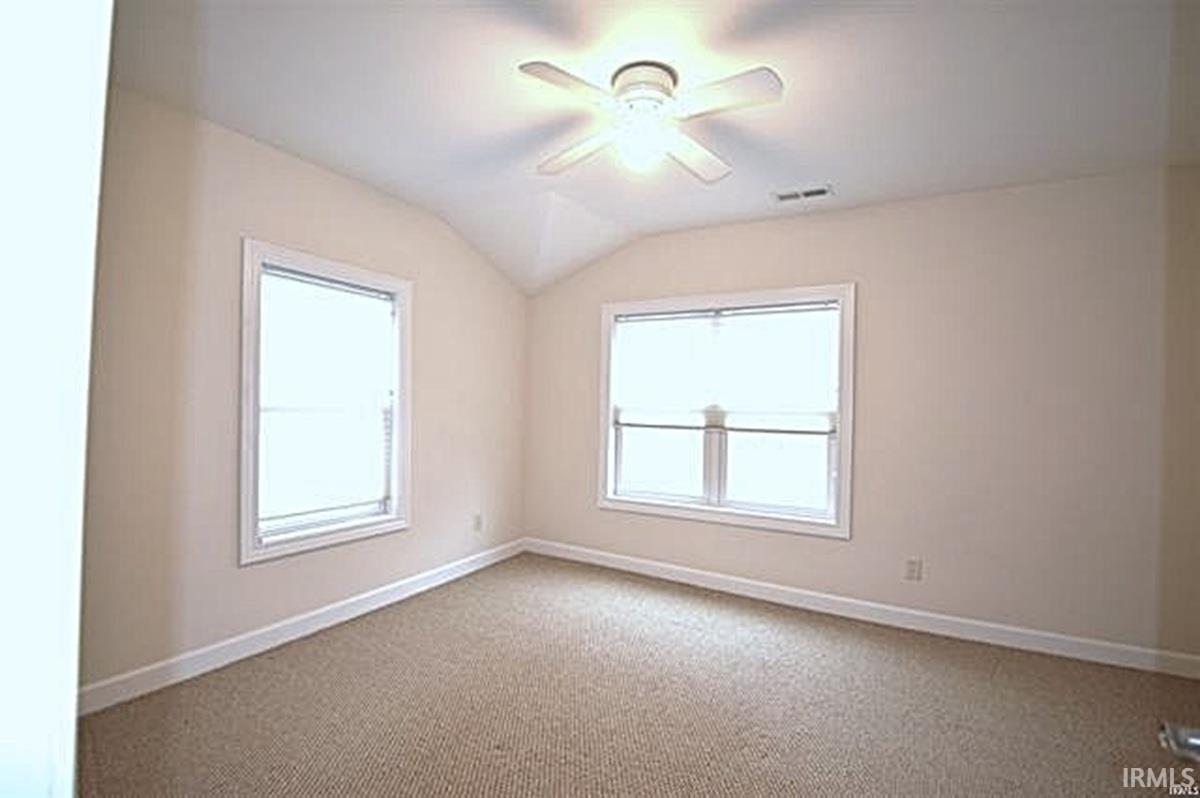Empty room with a ceiling fan, carpet floors, lofted ceiling, and plenty of natural light
