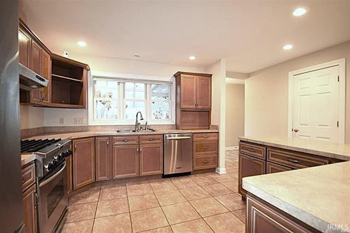 Kitchen featuring stainless steel appliances, light countertops, recessed lighting, light tile patterned flooring, and range hood