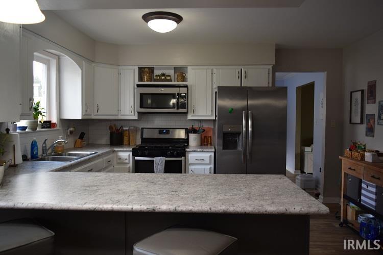 Kitchen with stainless steel appliances, a peninsula, tasteful backsplash, white cabinets, and a breakfast bar area