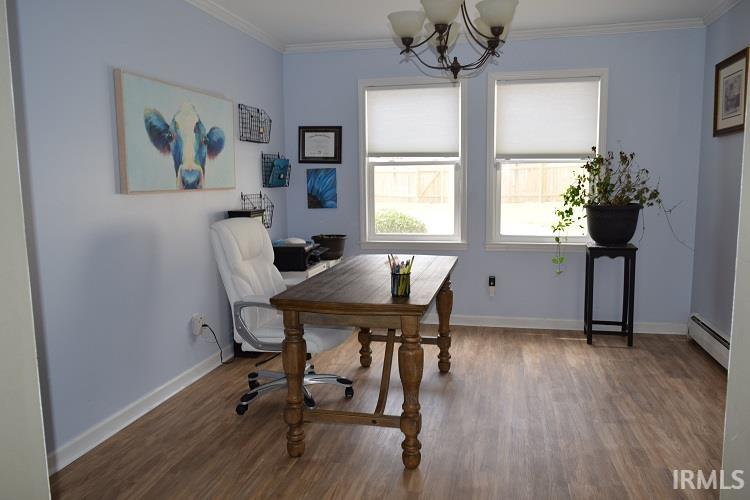 Dining space featuring dark wood-type flooring, a baseboard radiator, ornamental molding, a desk, and a chandelier