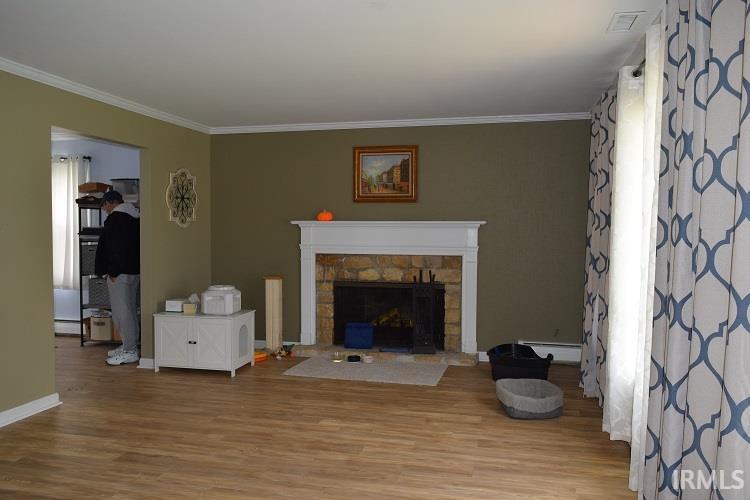 Living room with wood finished floors, a stone fireplace, and crown molding