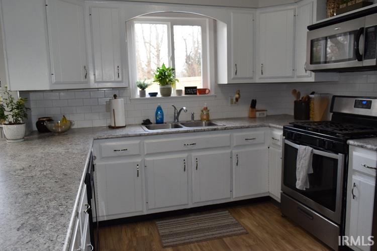 Kitchen with stainless steel appliances, white cabinetry, light countertops, and dark wood-style floors
