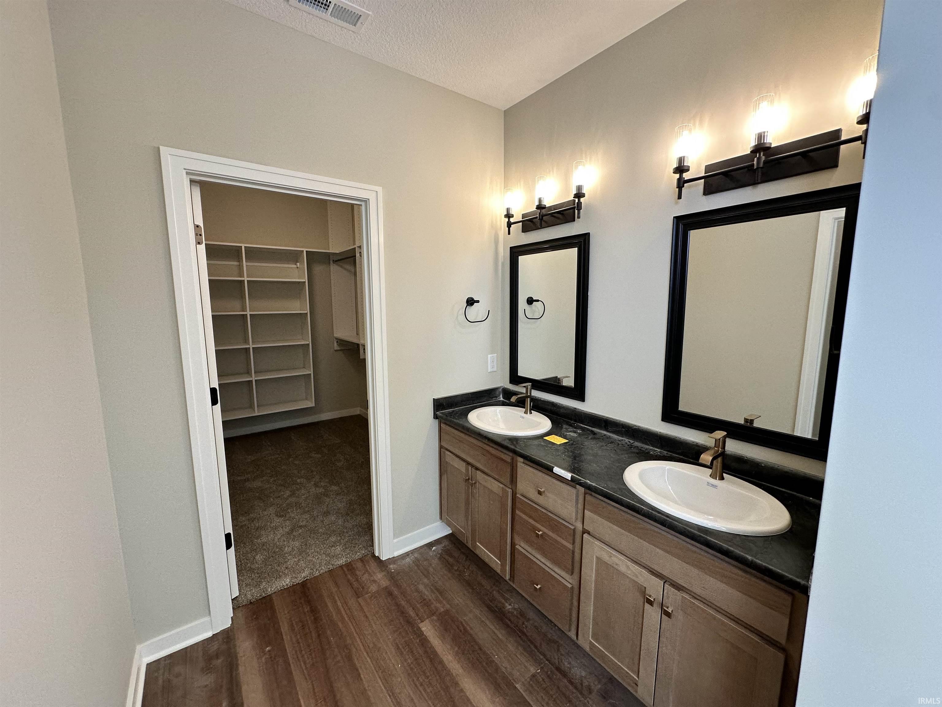 Full bath featuring a spacious closet, double vanity, dark wood finished floors, and a textured ceiling