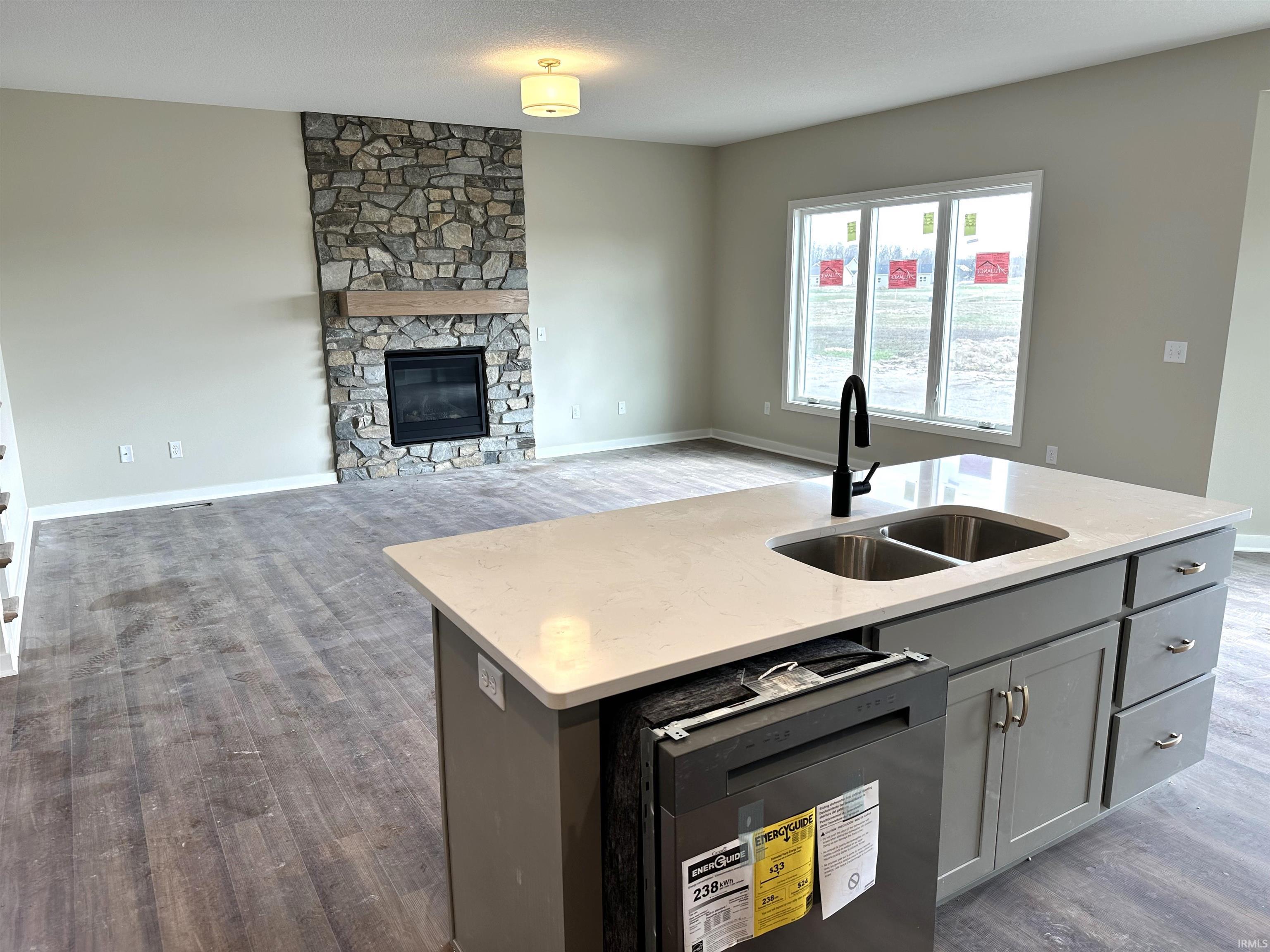 Kitchen featuring a stone fireplace, dark wood finished floors, stainless steel dishwasher, light stone counters, and gray cabinets