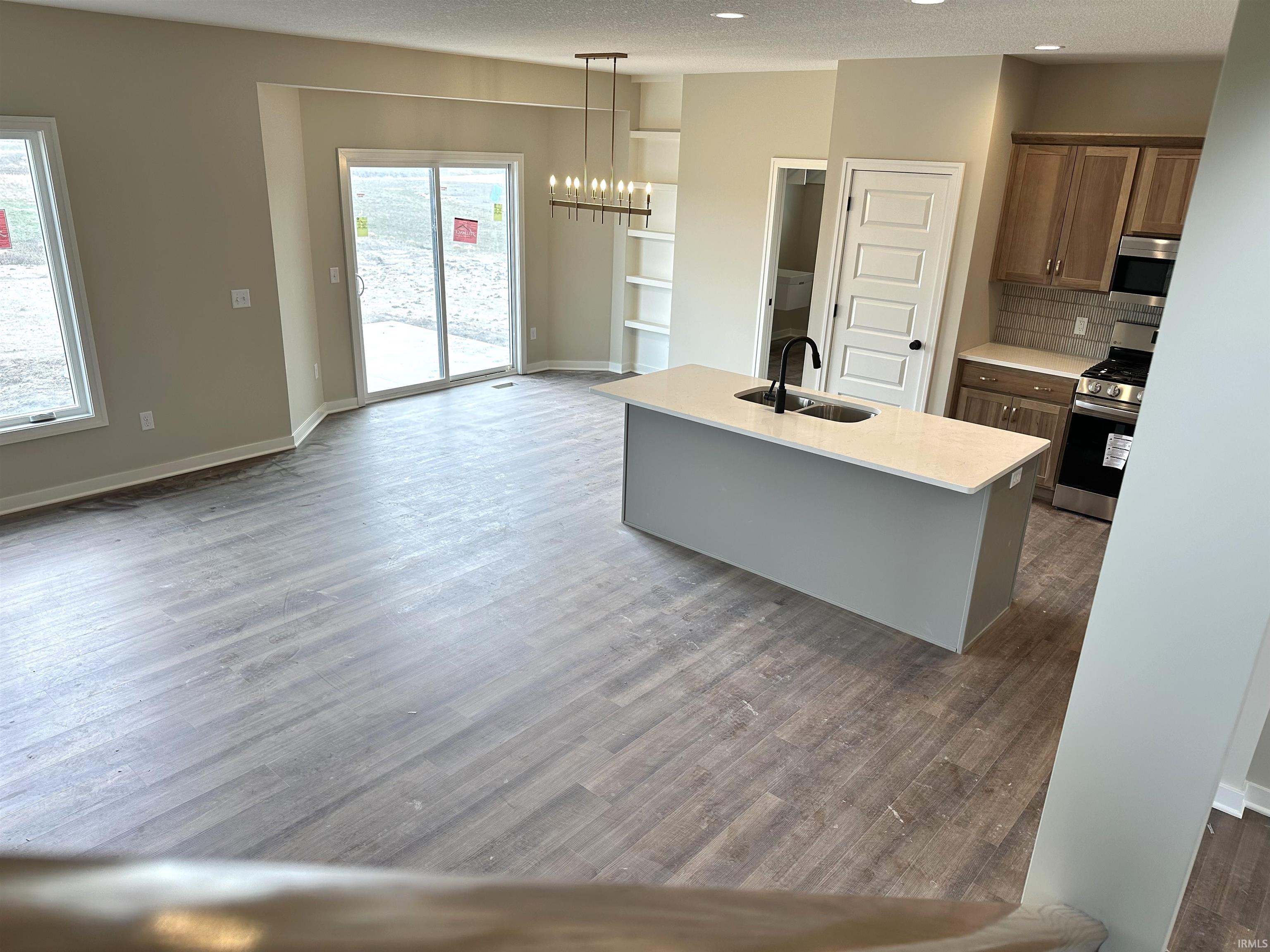 Kitchen with stainless steel appliances, hanging lights, an island with sink, dark wood finished floors, and a textured ceiling