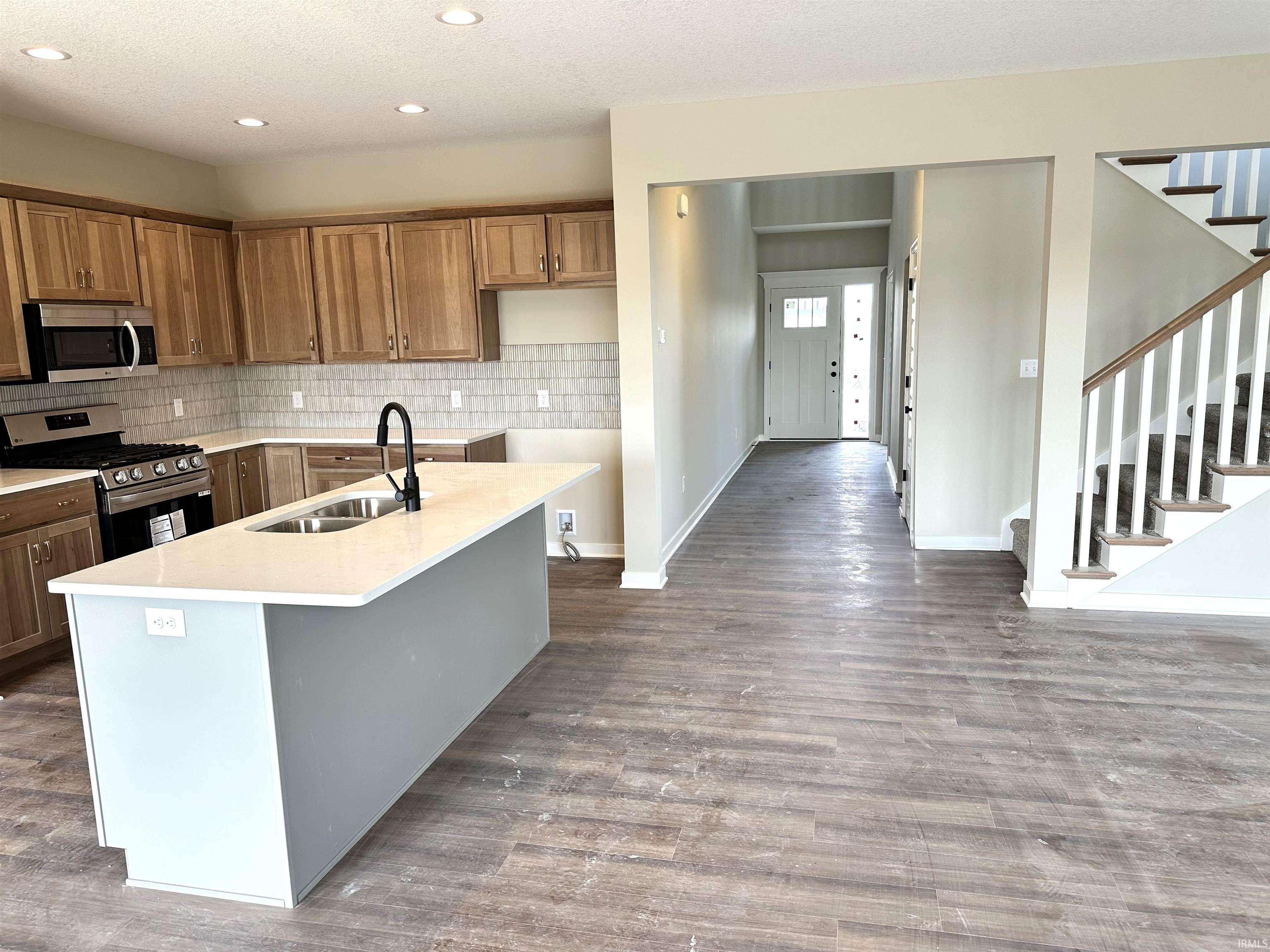 Kitchen featuring stainless steel appliances, wood finish cabinets, an island with sink, recessed lighting, and light stone countertops