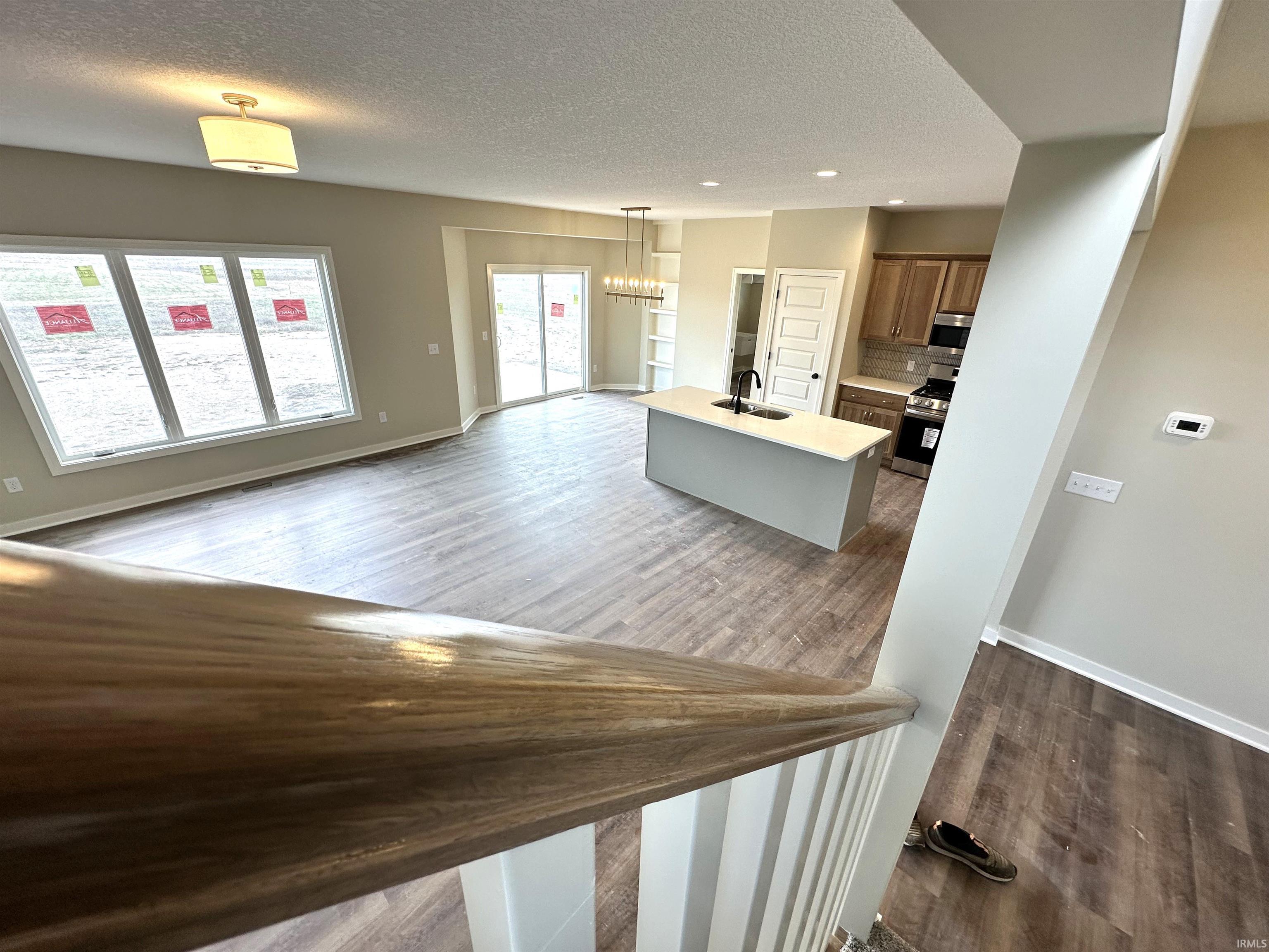 Kitchen with a chandelier, a center island with sink, dark wood-type flooring, stainless steel appliances, and a textured ceiling