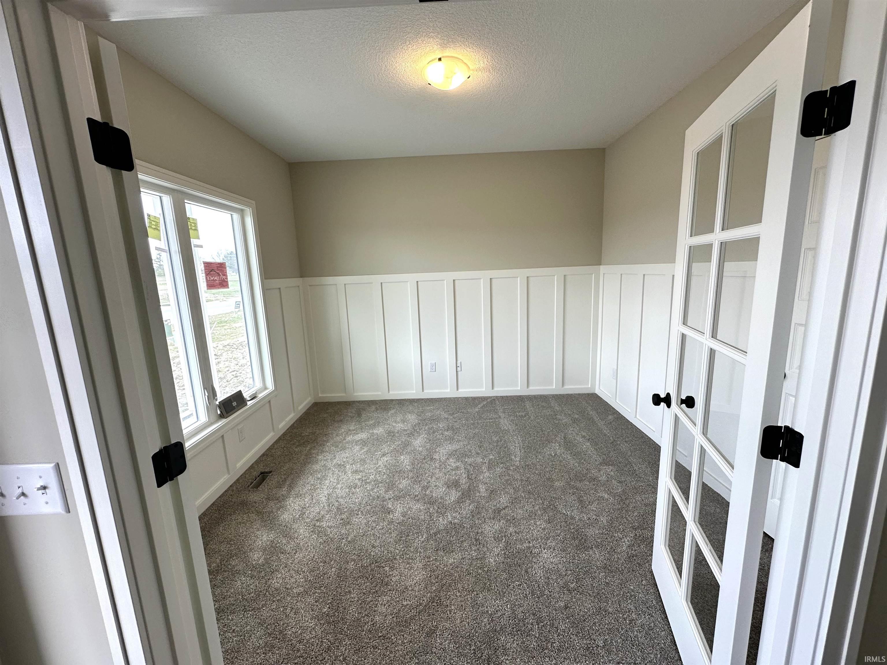 Unfurnished room with a decorative wall, a wainscoted wall, dark carpet, and a textured ceiling