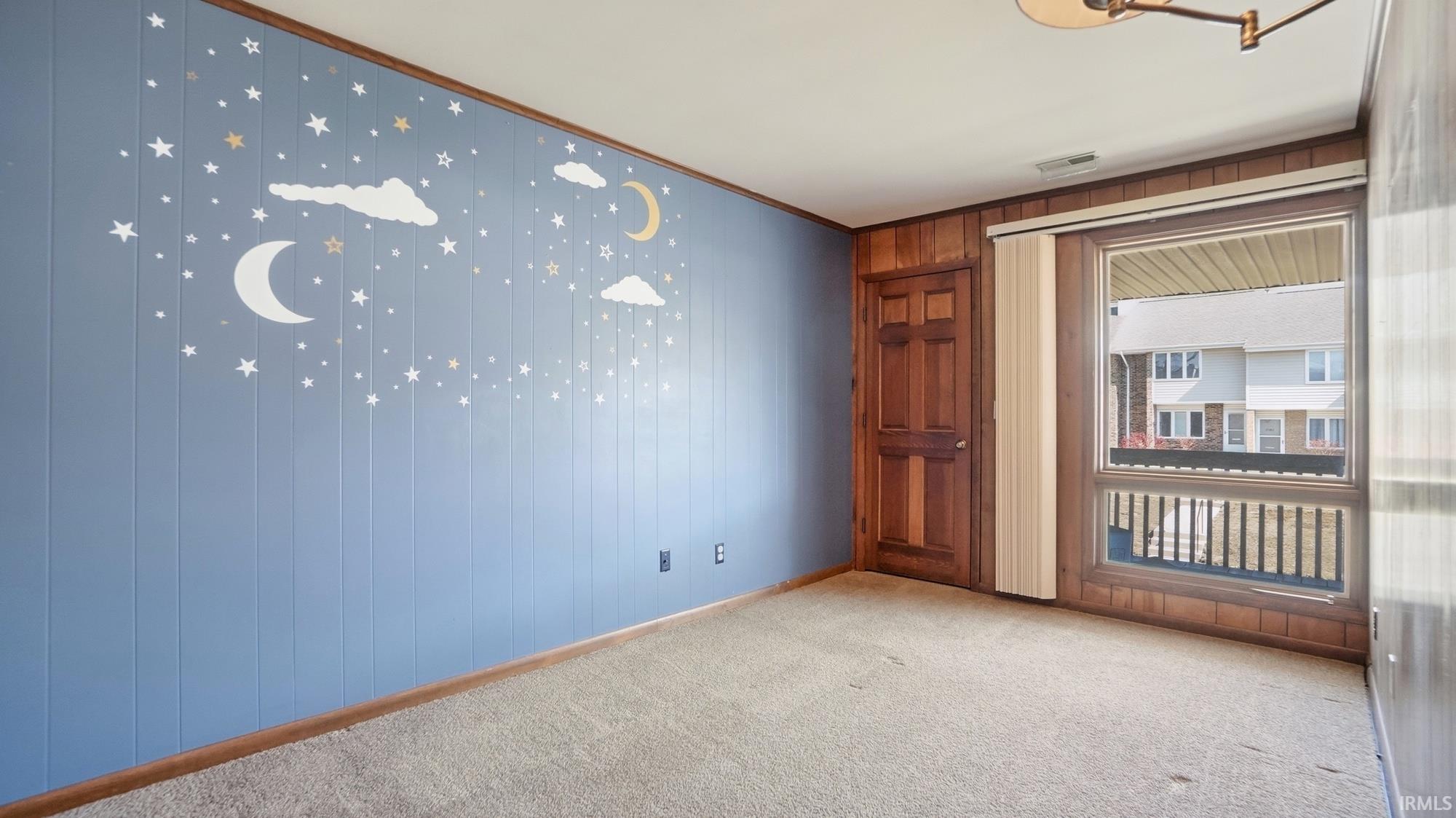 Unfurnished room featuring wooden walls, ornamental molding, and light colored carpet