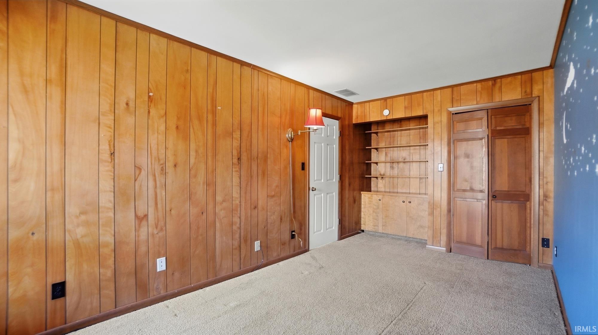 Unfurnished bedroom with a closet, carpet, and wooden walls