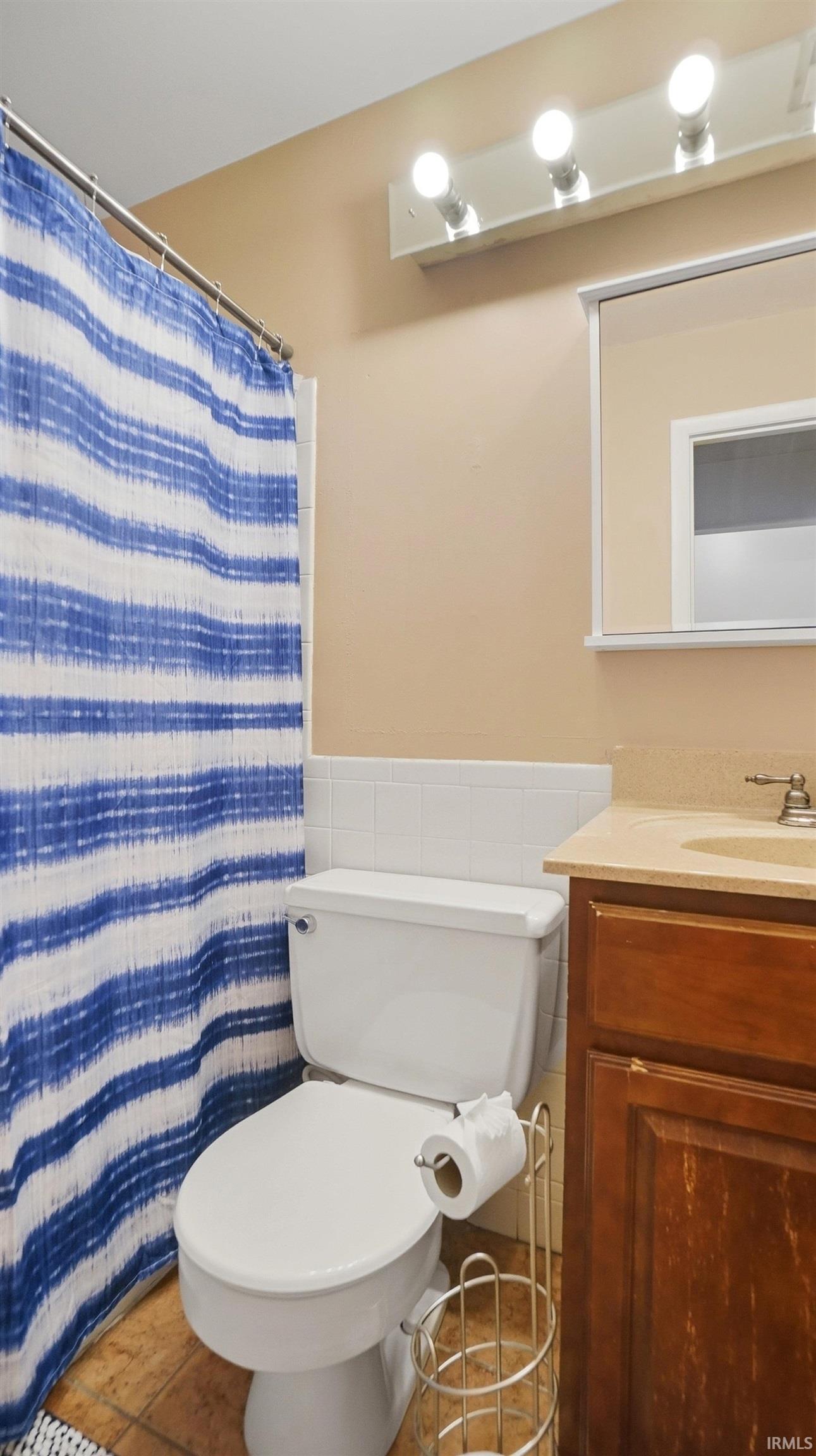 Full bath featuring vanity, a shower with curtain, wainscoting, tile walls, and tile patterned flooring