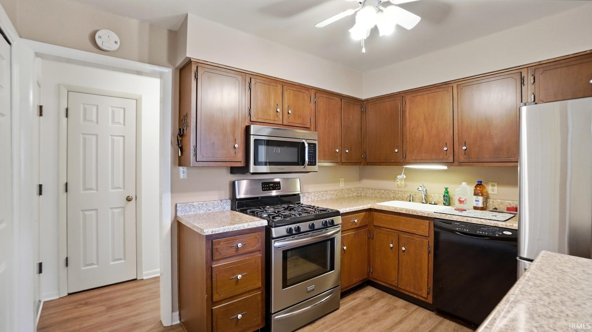 Kitchen featuring stainless steel appliances, light countertops, ceiling fan, light wood-style flooring, and wood finish cabinetry