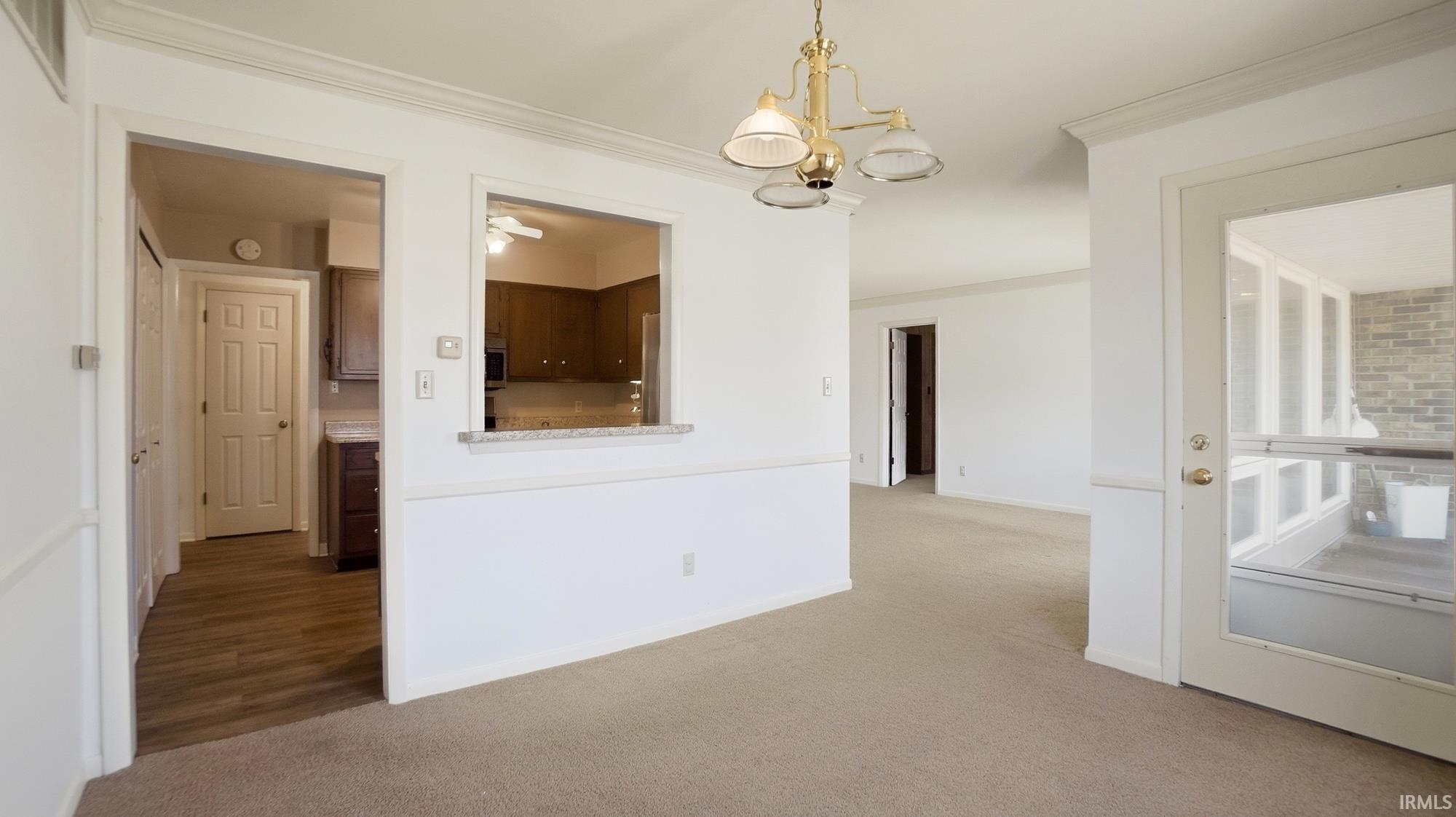 Carpeted spare room featuring crown molding and hanging lights