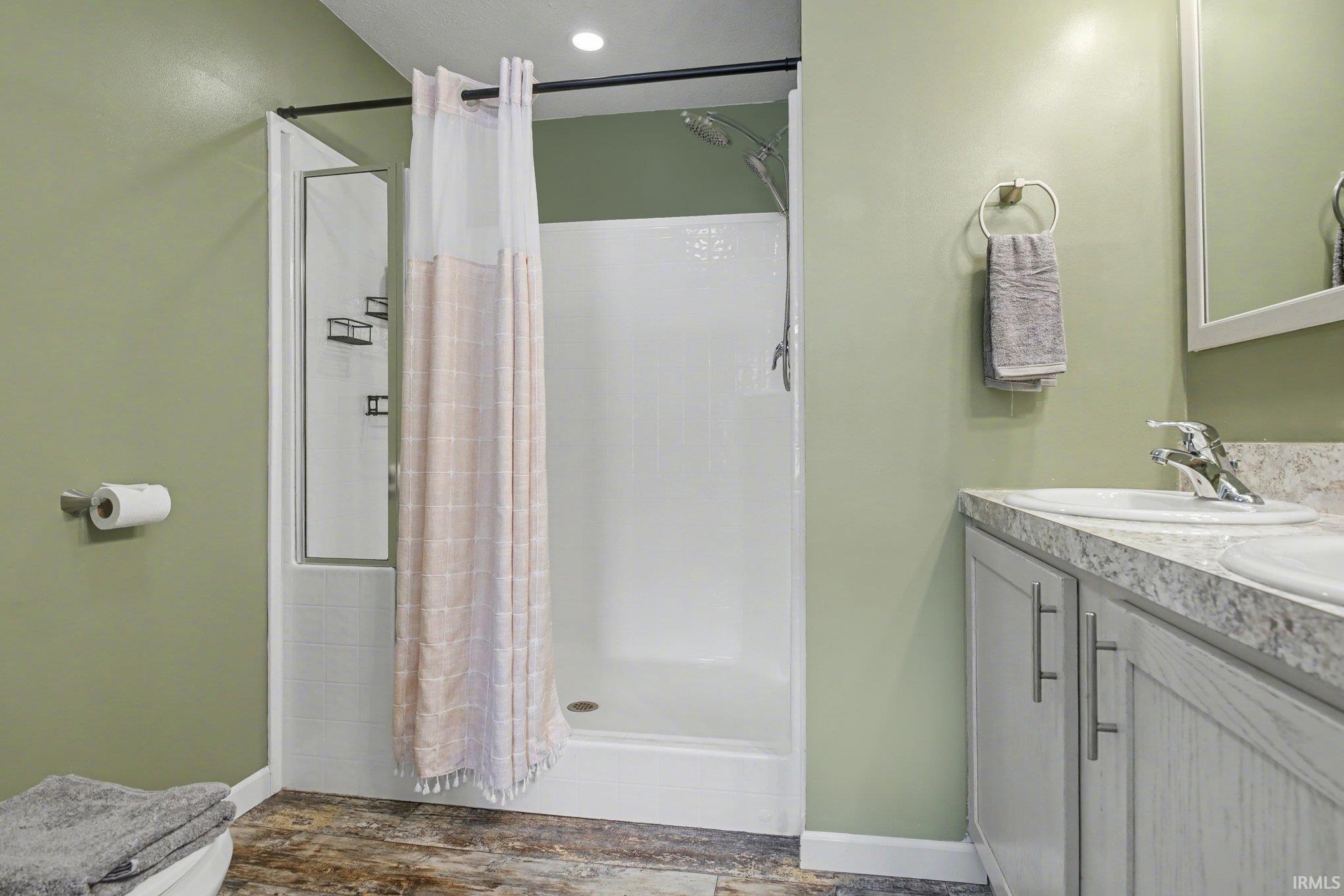 Bathroom featuring double vanity, a shower stall, and dark wood-style floors