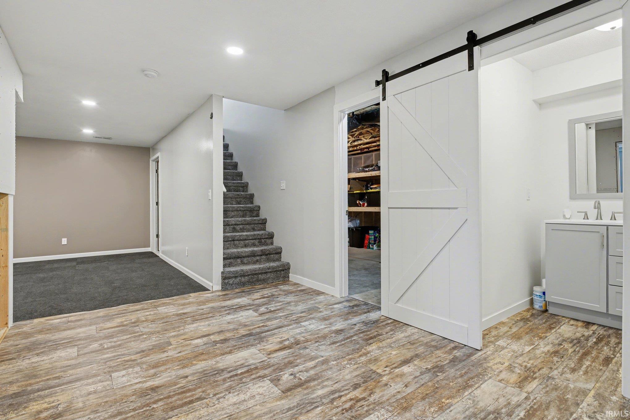 Finished below grade area featuring a barn door, dark wood finished floors, and recessed lighting