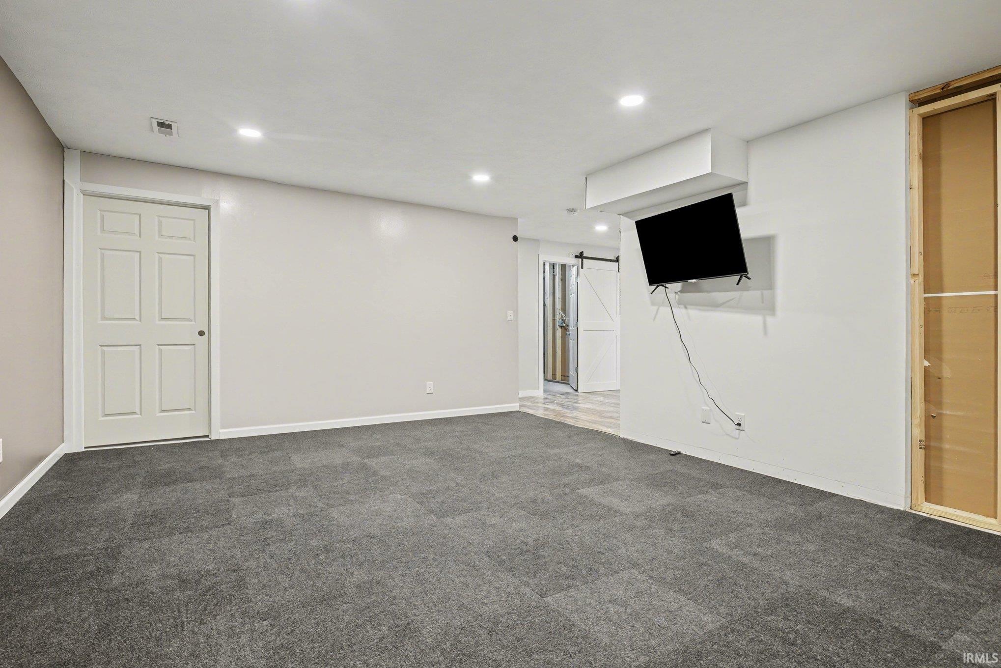 Basement featuring dark carpet, a barn door, and recessed lighting