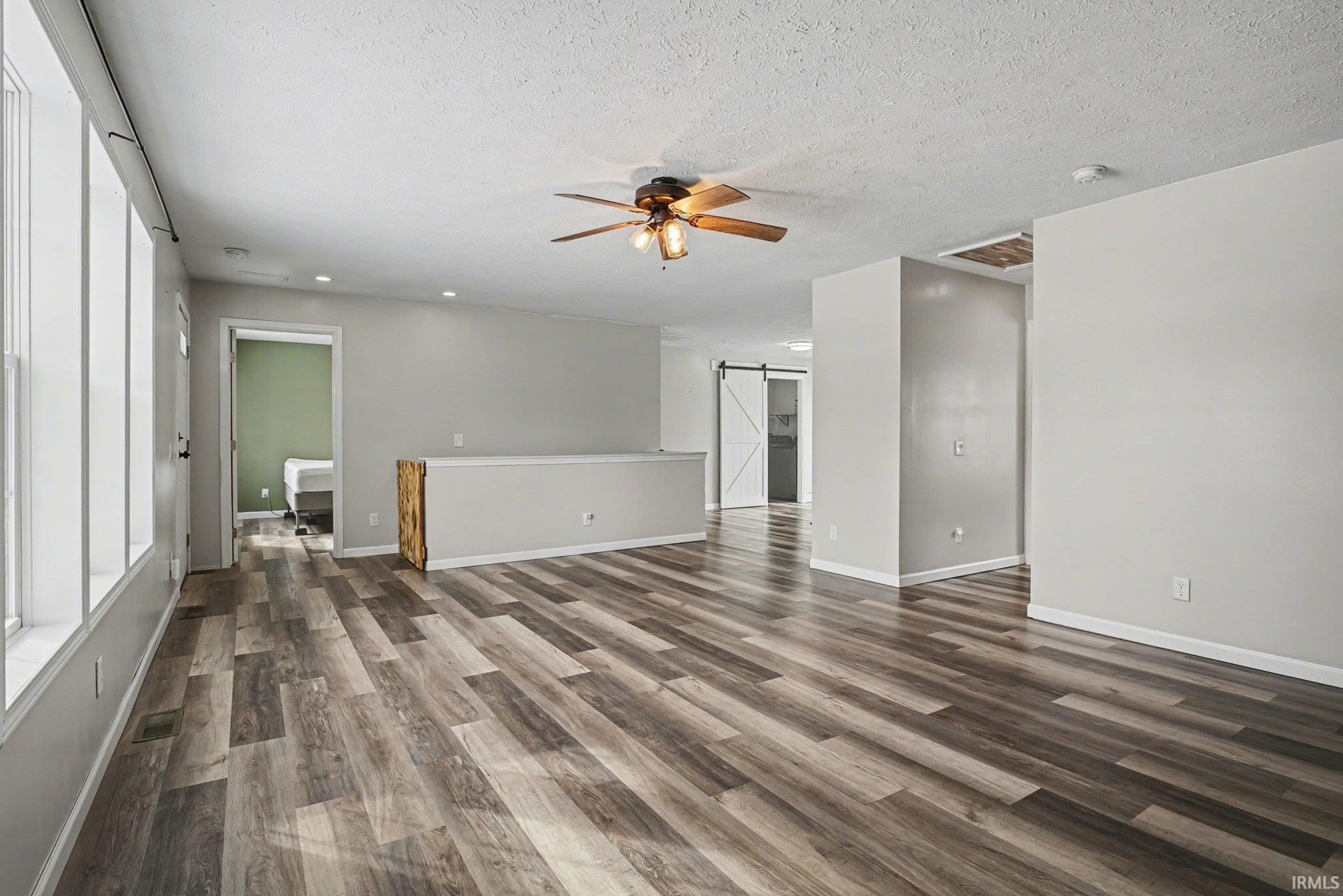 Unfurnished living room featuring a barn door, ceiling fan, dark wood finished floors, and a textured ceiling