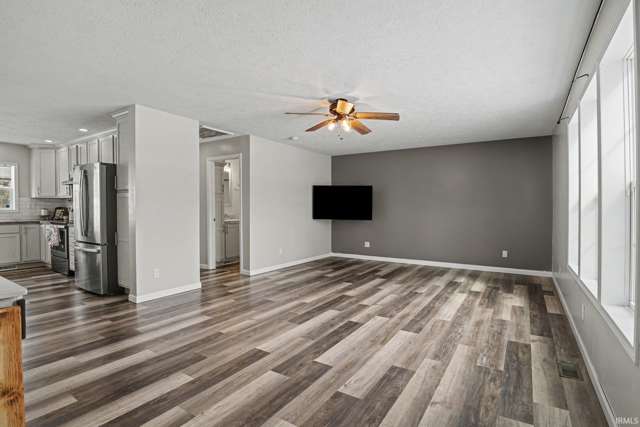 Unfurnished living room with ceiling fan, dark wood-style floors, and a textured ceiling