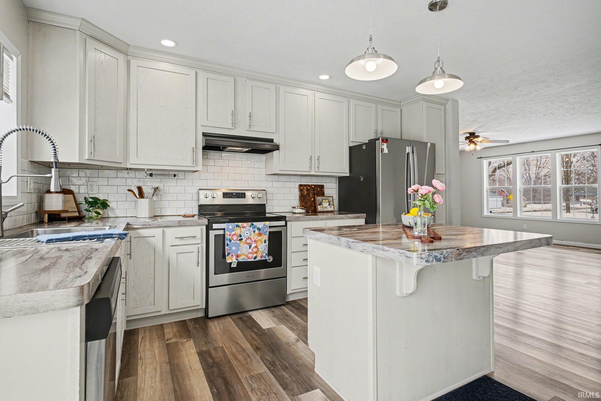 Kitchen with stainless steel appliances, a kitchen bar, dark wood-style floors, a center island, and hanging light fixtures