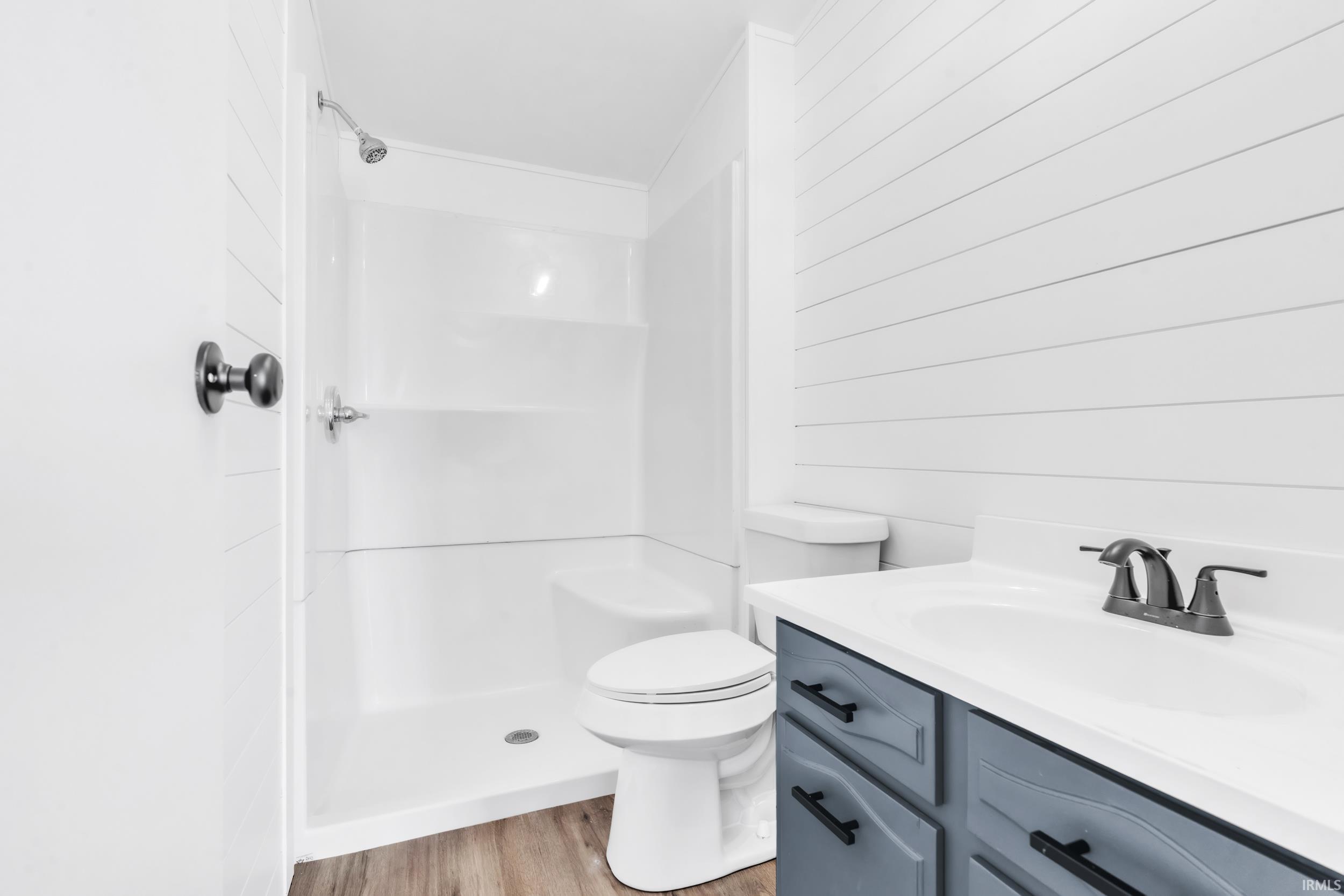 Full bath featuring vanity, a shower stall, light wood-type flooring, and wooden walls