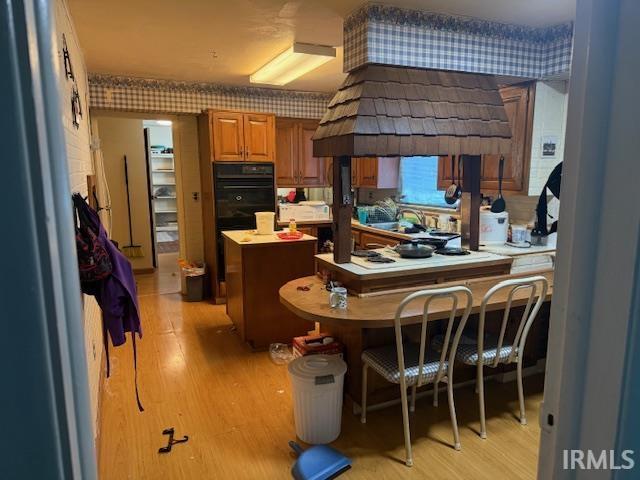 Kitchen featuring a peninsula, wood finish cabinets, light wood-style flooring, a kitchen breakfast bar, and light countertops
