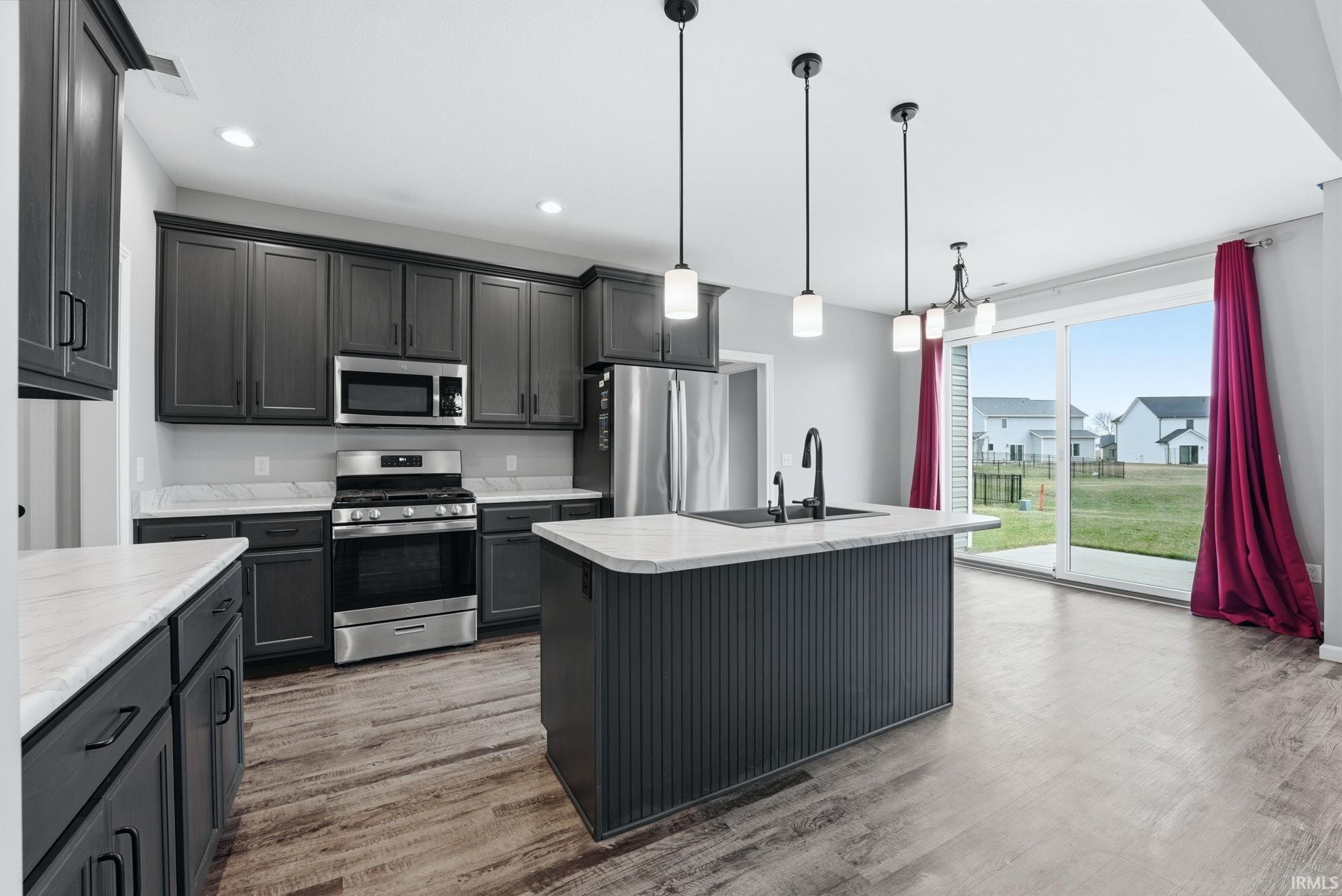 Kitchen with stainless steel appliances, light countertops, a center island with sink, and decorative light fixtures