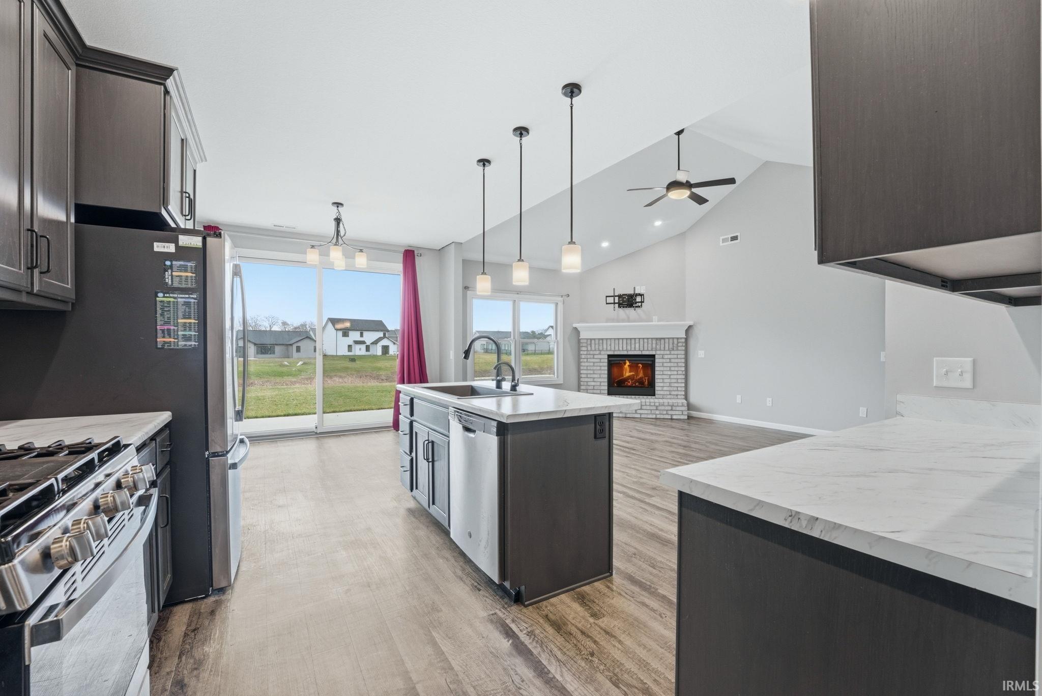 Kitchen with open floor plan, an island with sink, light wood-style floors, a fireplace, and lofted ceiling