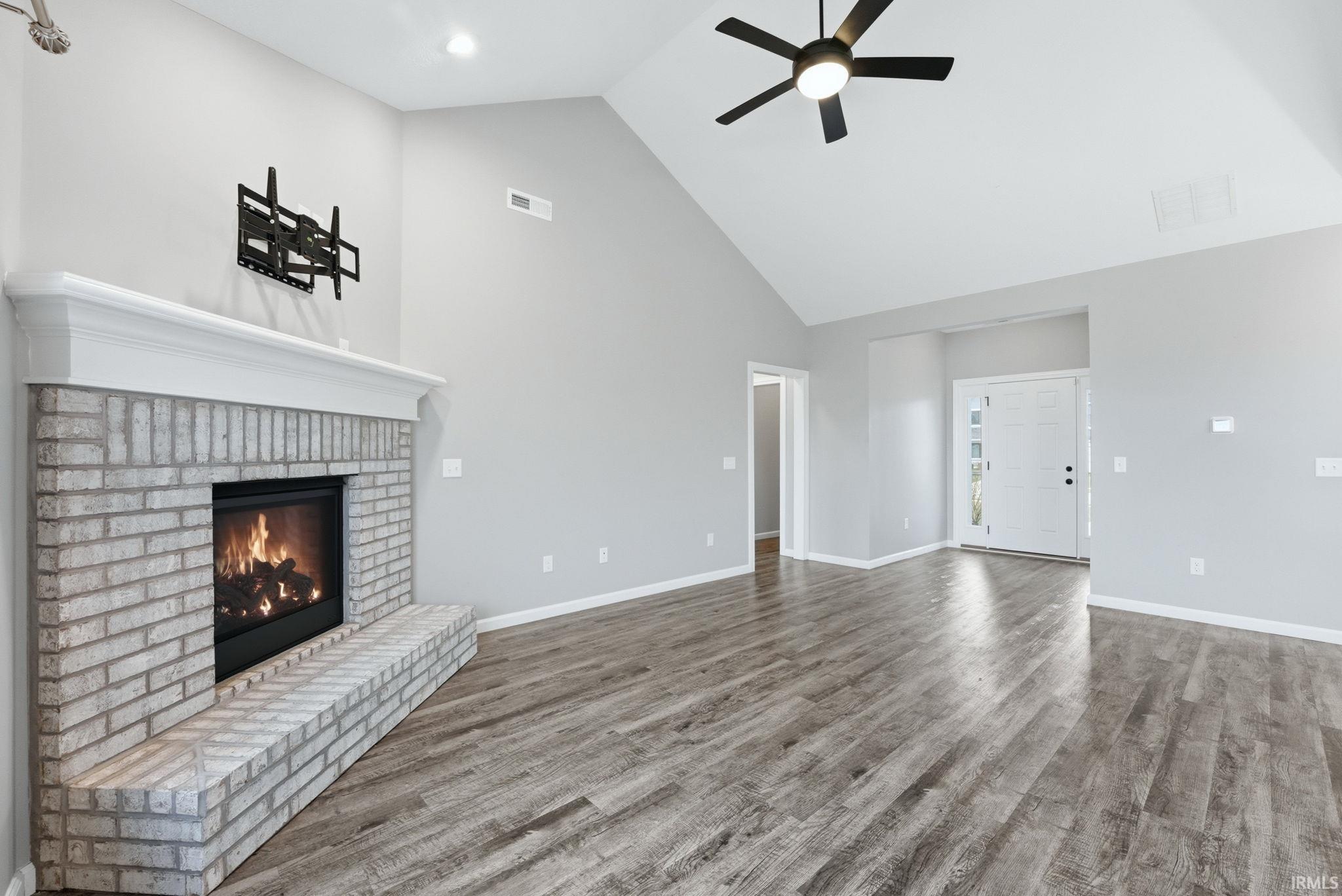 Unfurnished living room featuring a high ceiling, a fireplace, a ceiling fan, and wood finished floors