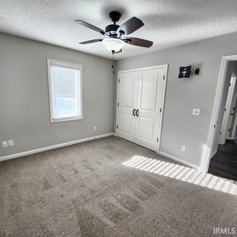 Unfurnished bedroom featuring a closet, carpet, a textured ceiling, and ceiling fan