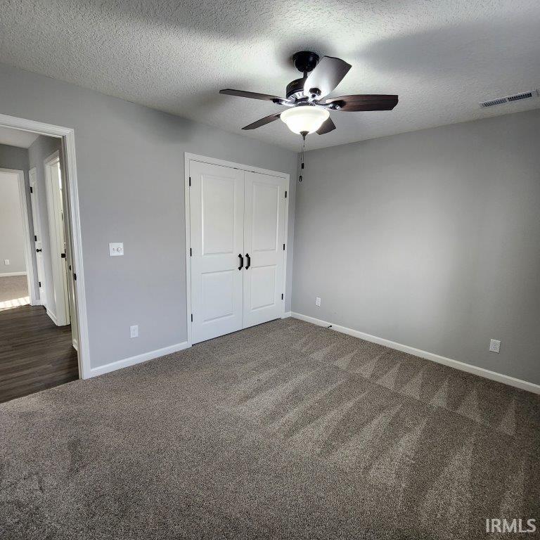 Unfurnished bedroom with dark colored carpet, a closet, a textured ceiling, and ceiling fan