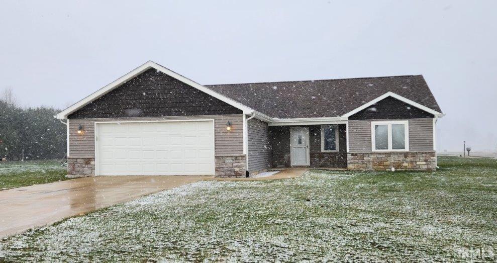Single story home featuring an attached garage, stone siding, driveway, and a front yard