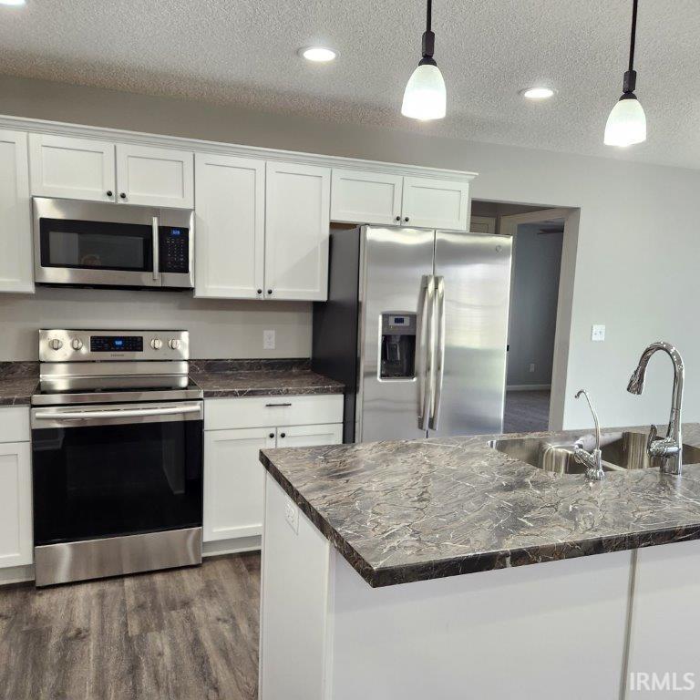 Kitchen with stainless steel appliances, white cabinetry, hanging light fixtures, dark wood-style floors, and a textured ceiling