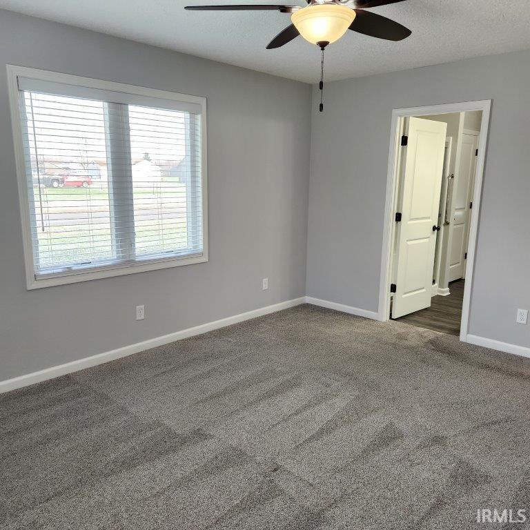 Empty room featuring ceiling fan, dark carpet, and a textured ceiling