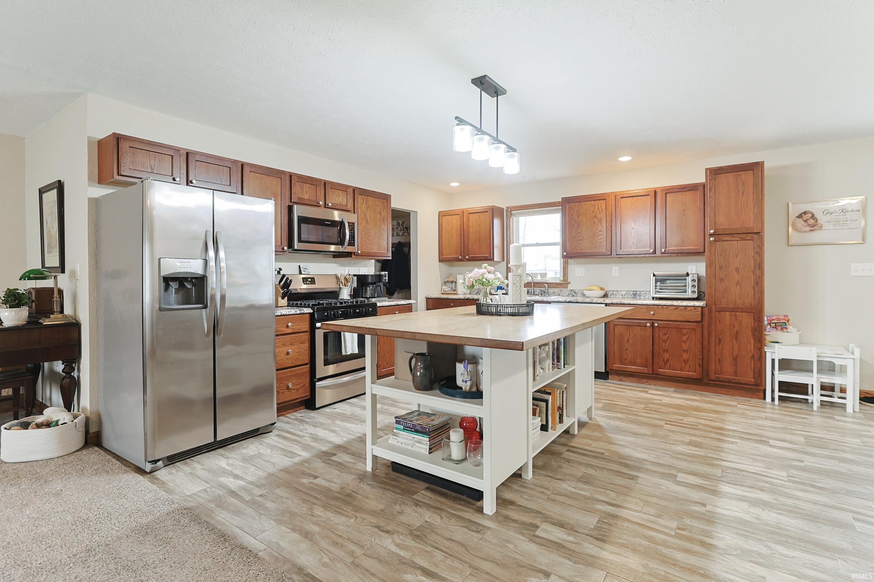 Kitchen featuring stainless steel appliances, wood finish cabinets, light wood-style flooring, pendant lighting, and open shelves