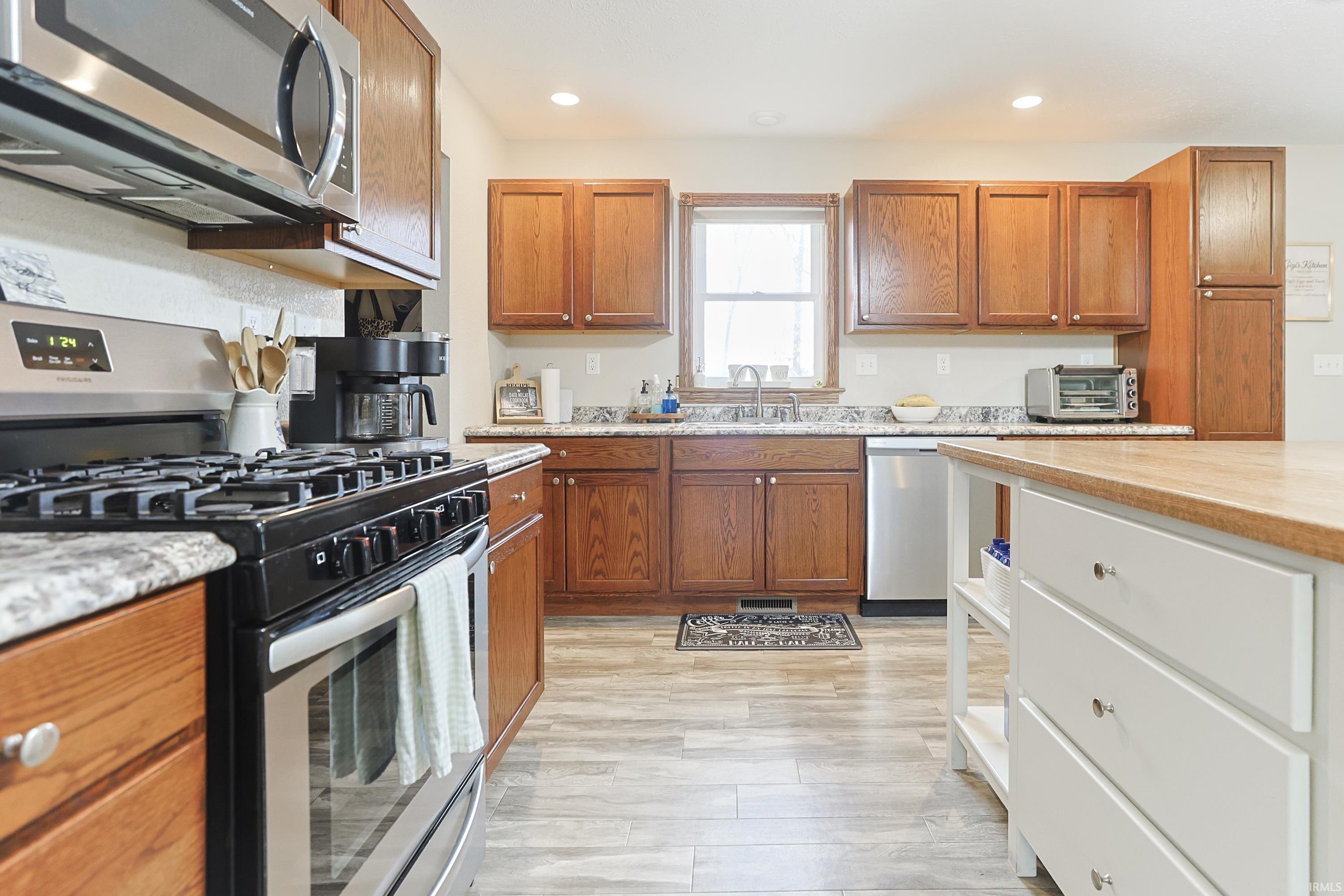 Two tone kitchen featuring stainless steel appliances, dual tone cabinetry, light stone countertops, recessed lighting, and light wood-style flooring