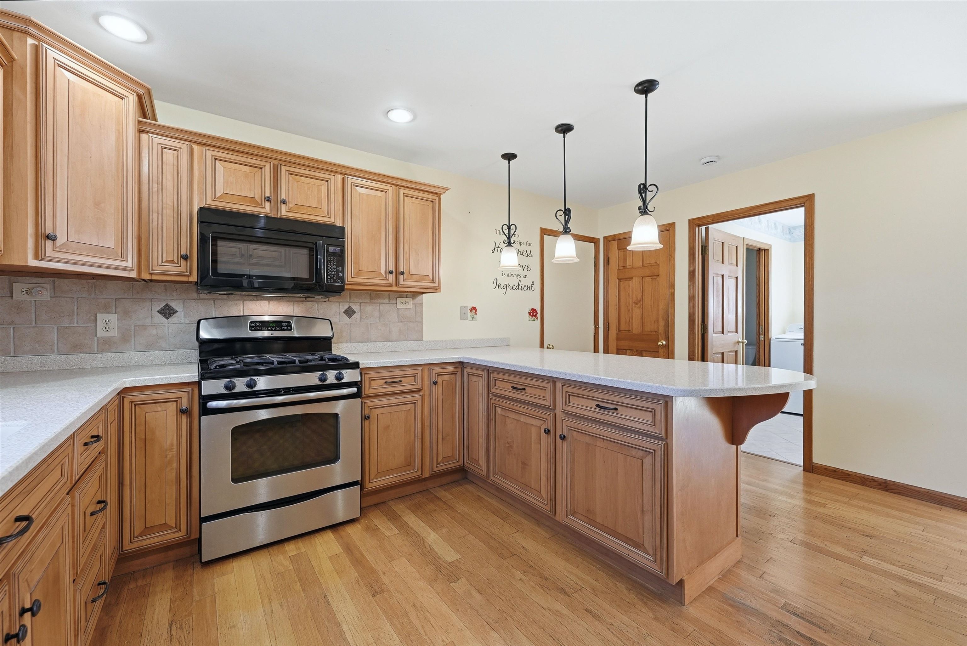 Kitchen with stainless steel gas range, a peninsula, black microwave, backsplash, custom cabinets with pull-out shelves