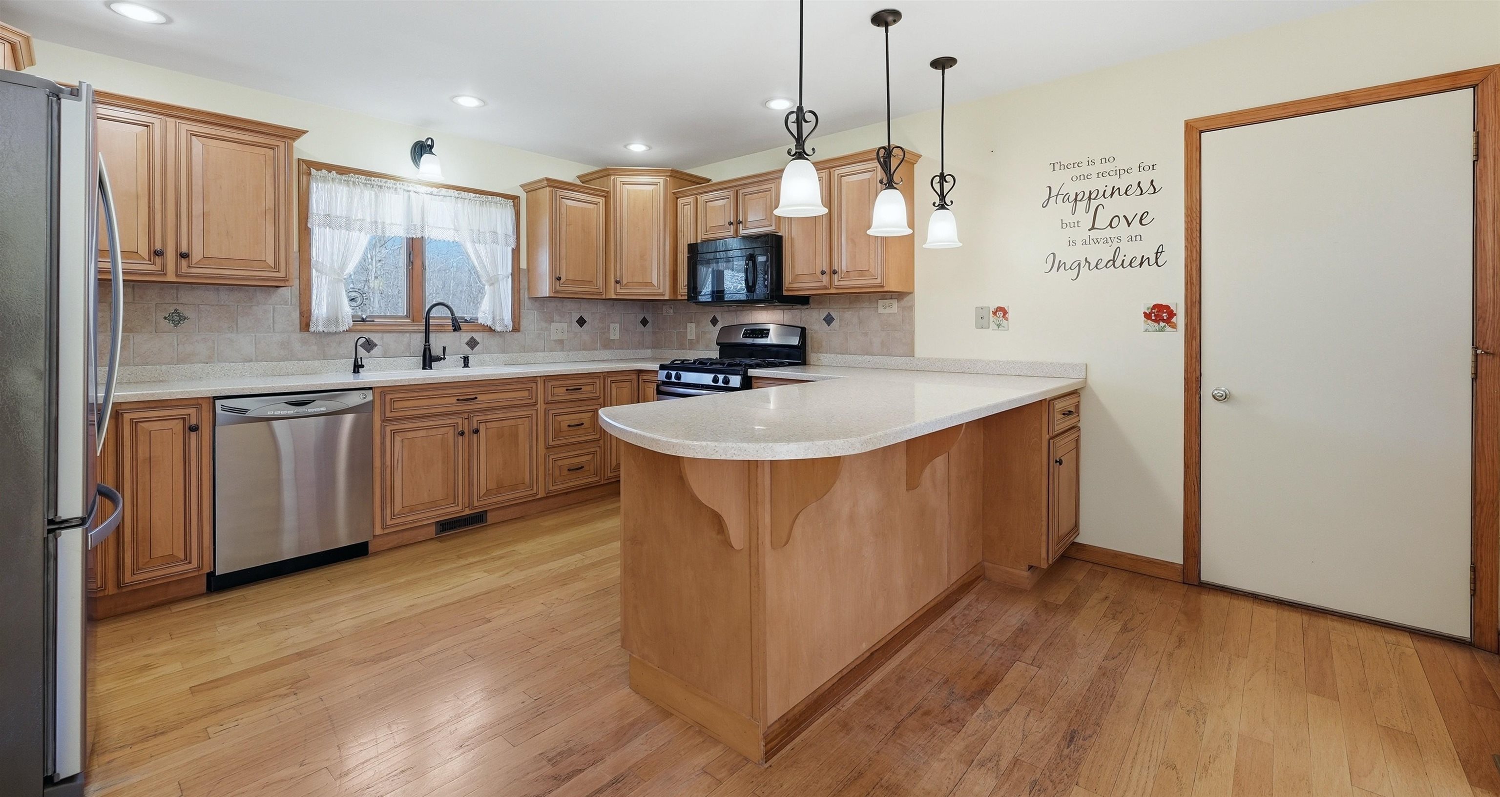Kitchen featuring a peninsula, stainless steel appliances, light wood flooring, pendant lighting, and tasteful backsplash