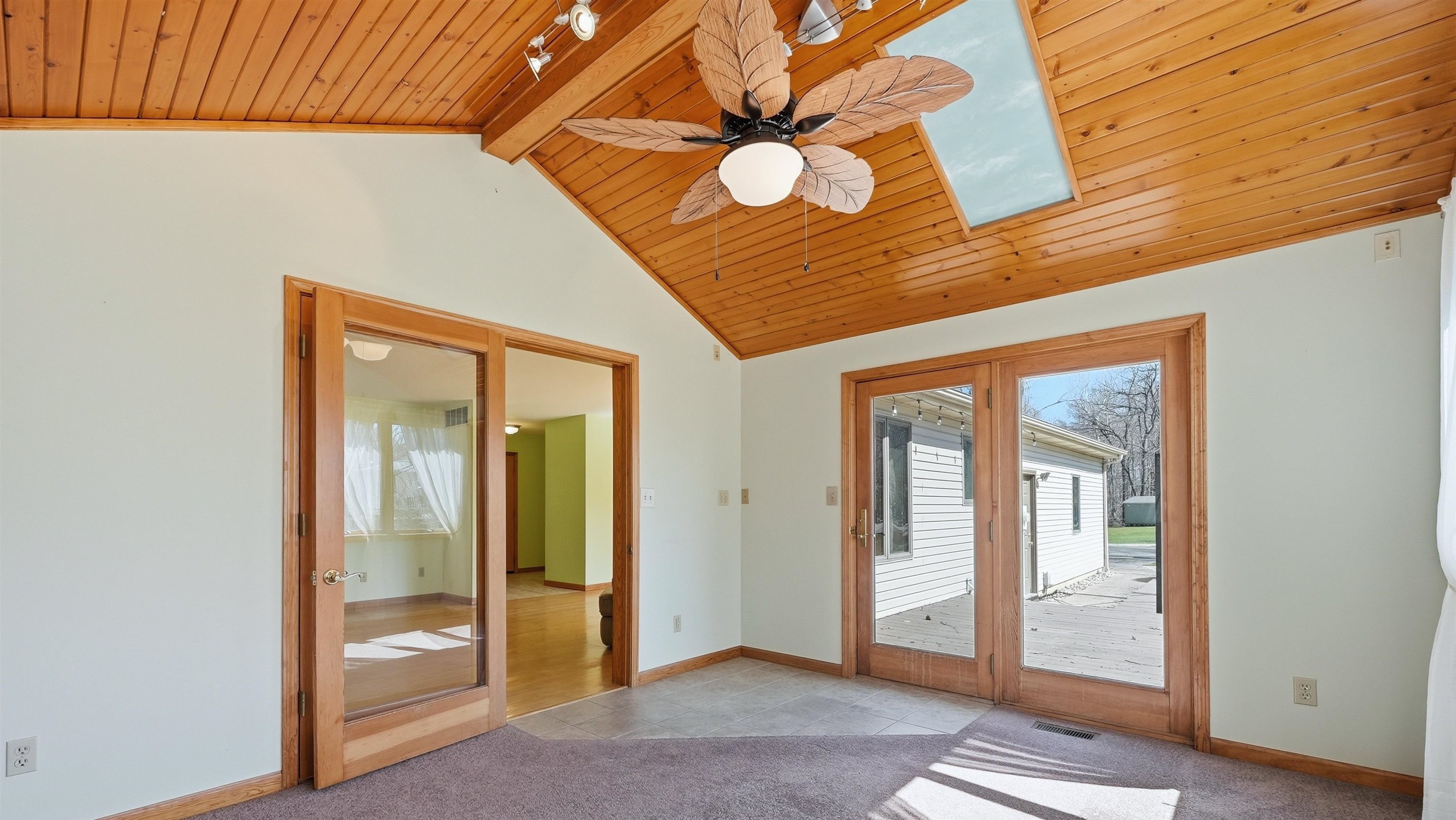 Sunroom with a wood ceiling with exposed beams, carpet floors, tile-patterned flooring, a ceiling fan, and a skylight