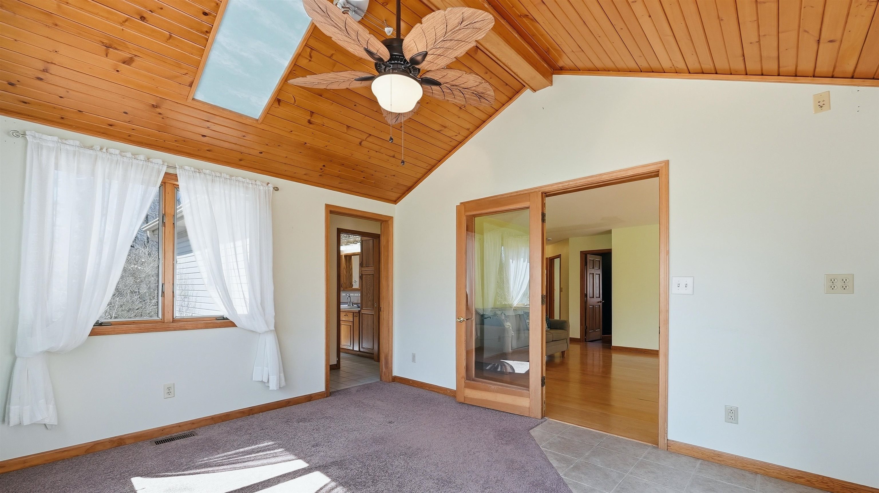 Sunroom entrance to owners suite featuring a ceiling fan, a wood ceiling with exposed beams, light colored carpet, and a skylight