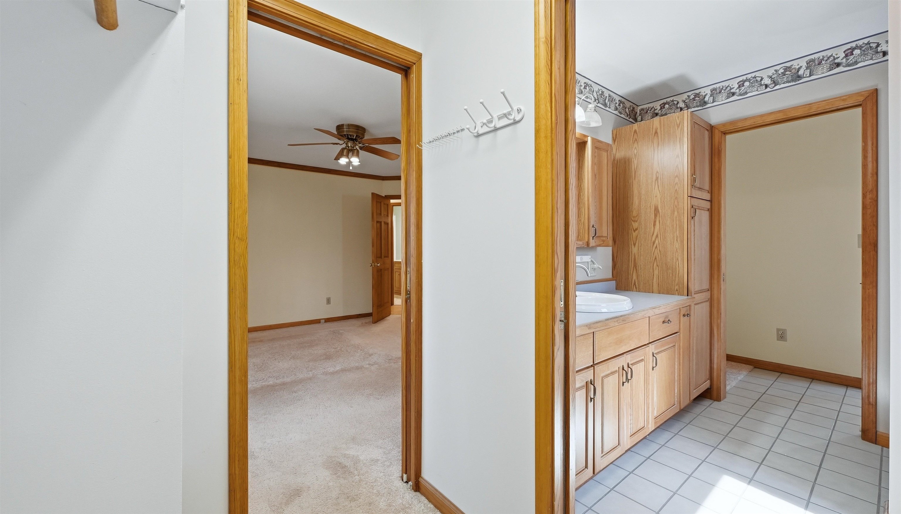 Bathroom featuring vanity, light colored carpet, ceiling fan, crown molding, and light tile patterned flooring