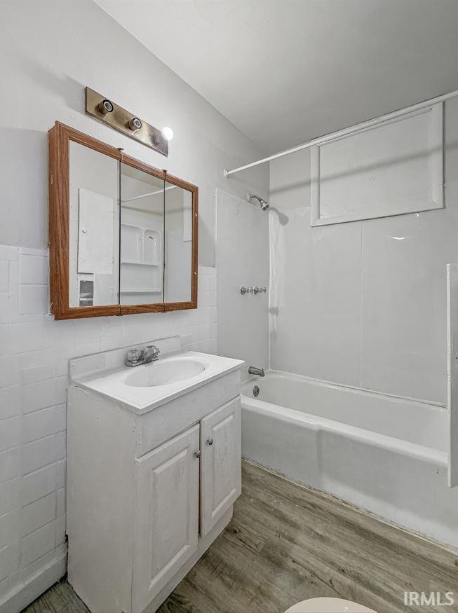 Bathroom featuring vanity, bathtub / shower combination, light wood-type flooring, and tile walls