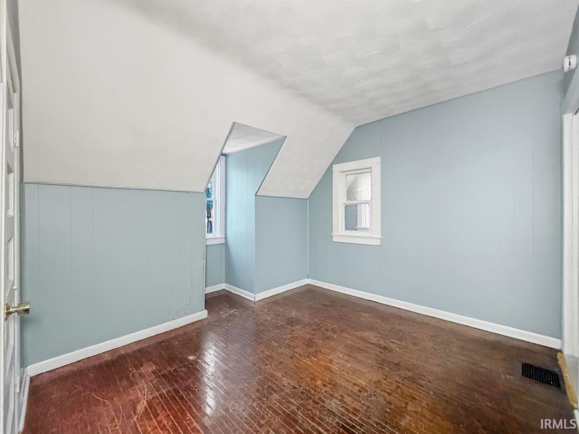 Additional living space with dark wood-style floors and vaulted ceiling
