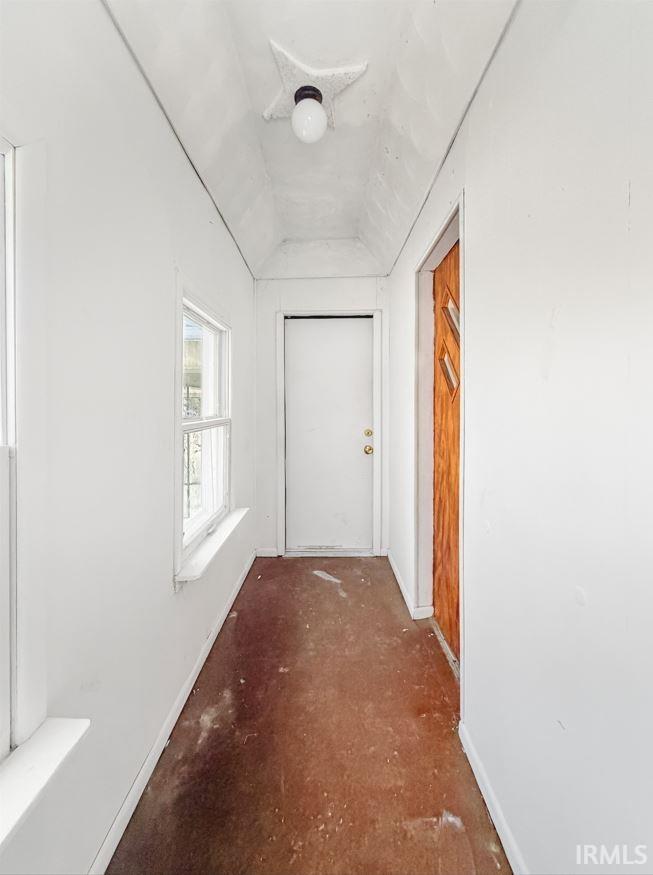 Hallway with vaulted ceiling and baseboards