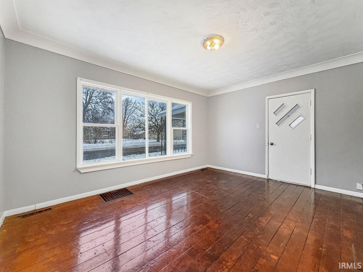 Empty room featuring dark wood-style flooring and crown molding