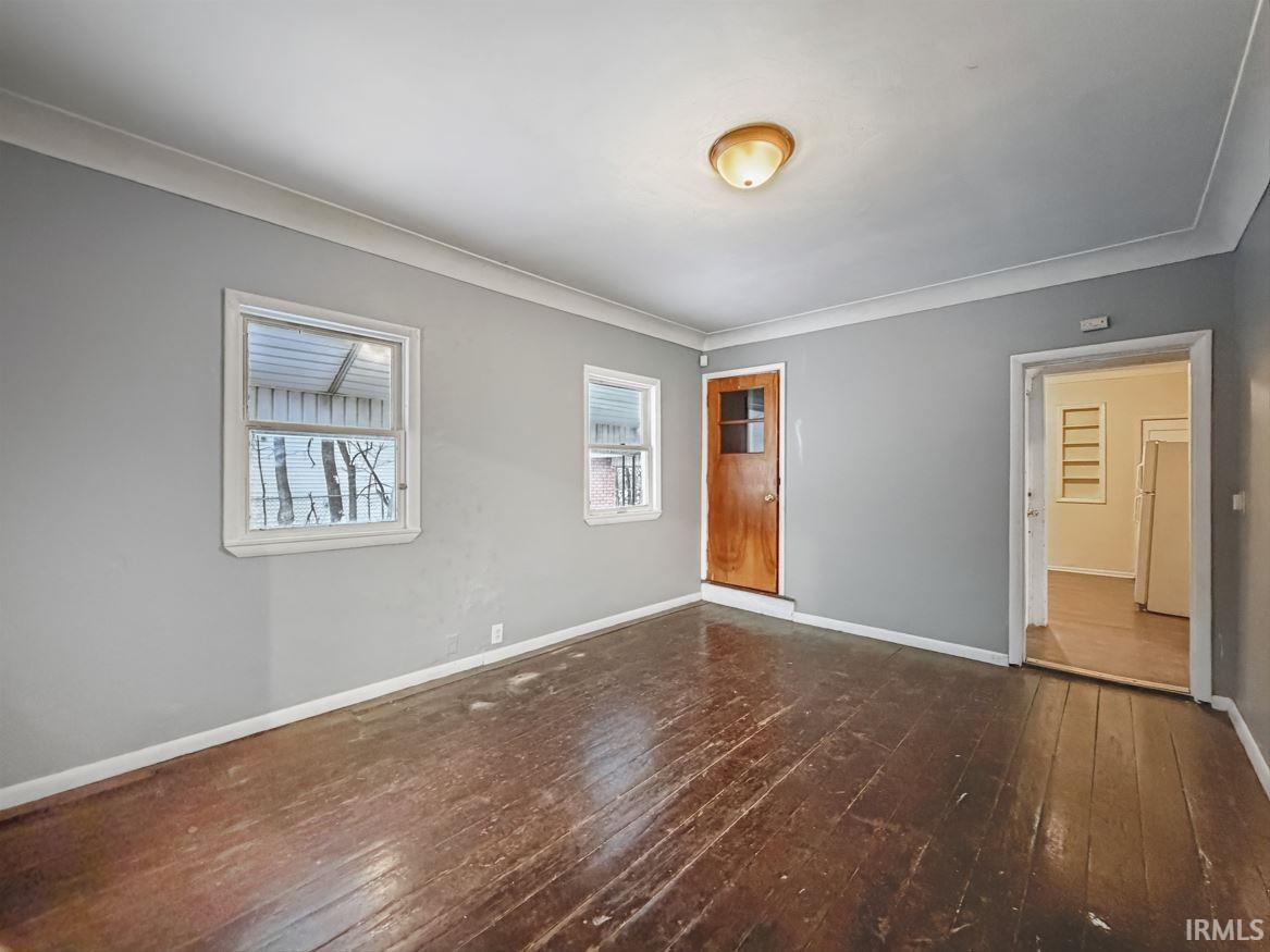 Unfurnished bedroom with dark wood-type flooring and freestanding refrigerator
