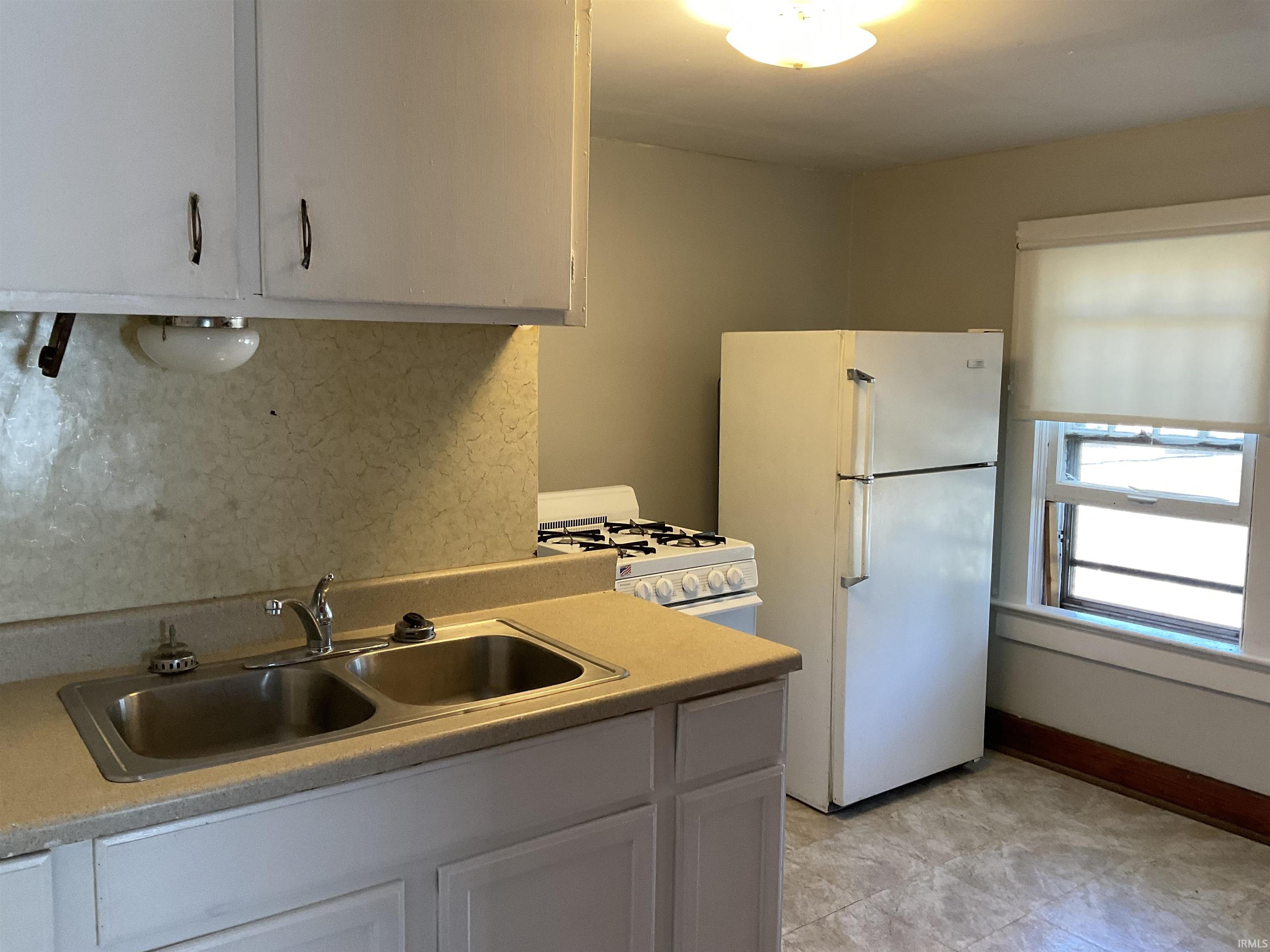 Kitchen featuring white appliances, light countertops, tasteful backsplash, and white cabinets